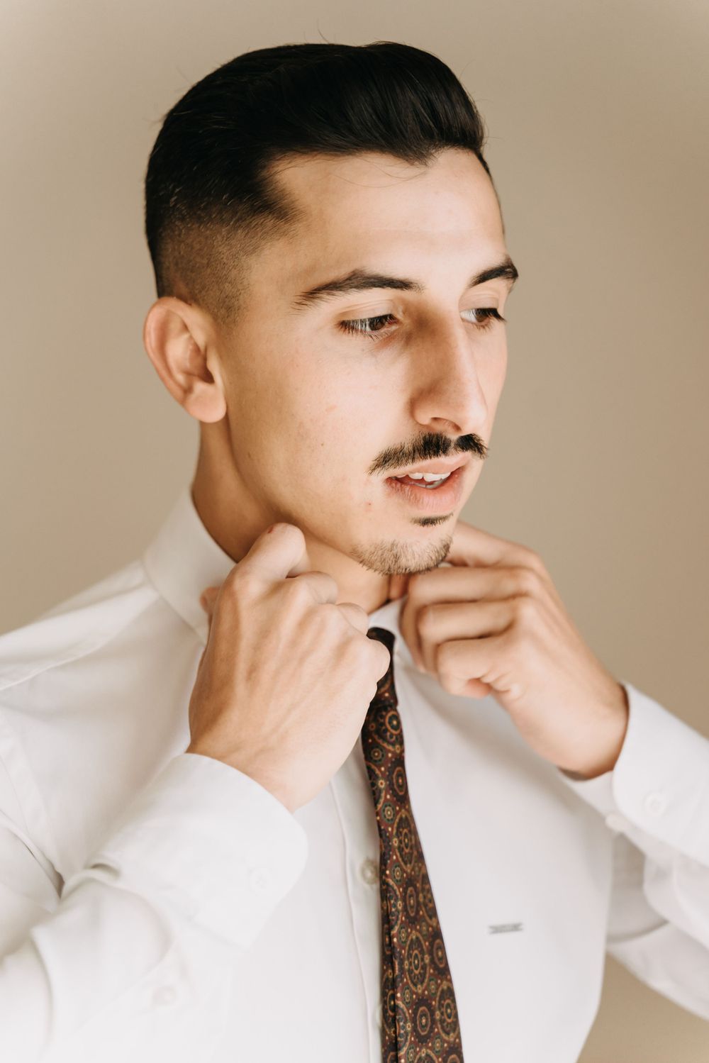Man adjusts his tie and collar while wearing a formal white shirt and patterned necktie.