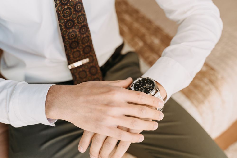 Close-up of wristwatch on hand against white shirt and patterned tie.