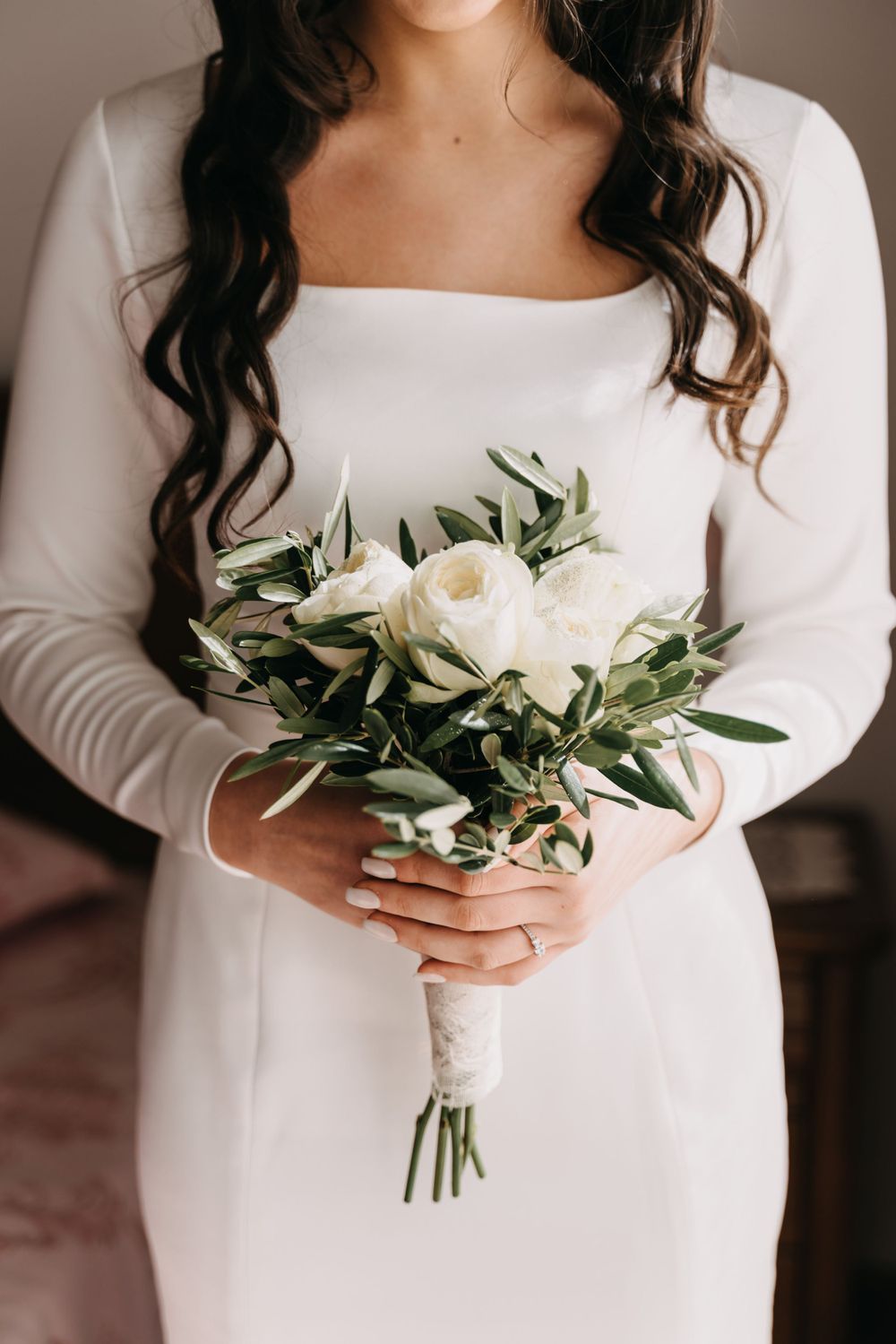 Close-up of white rose and greenery bouquet held against white wedding dress.