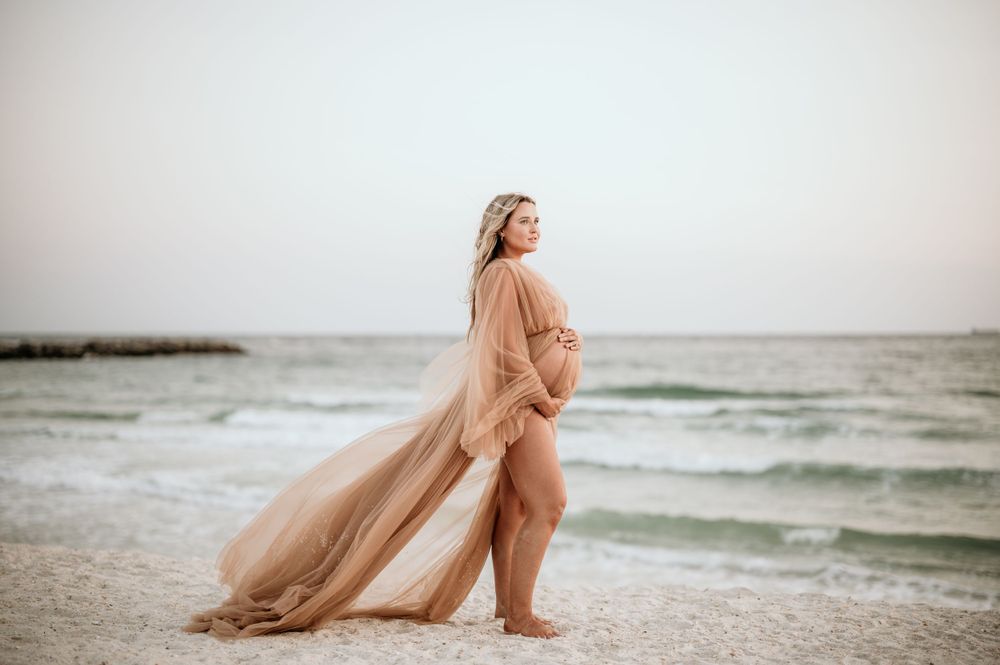 Maternity beach portrait with flowing peach dress catching the ocean breeze.