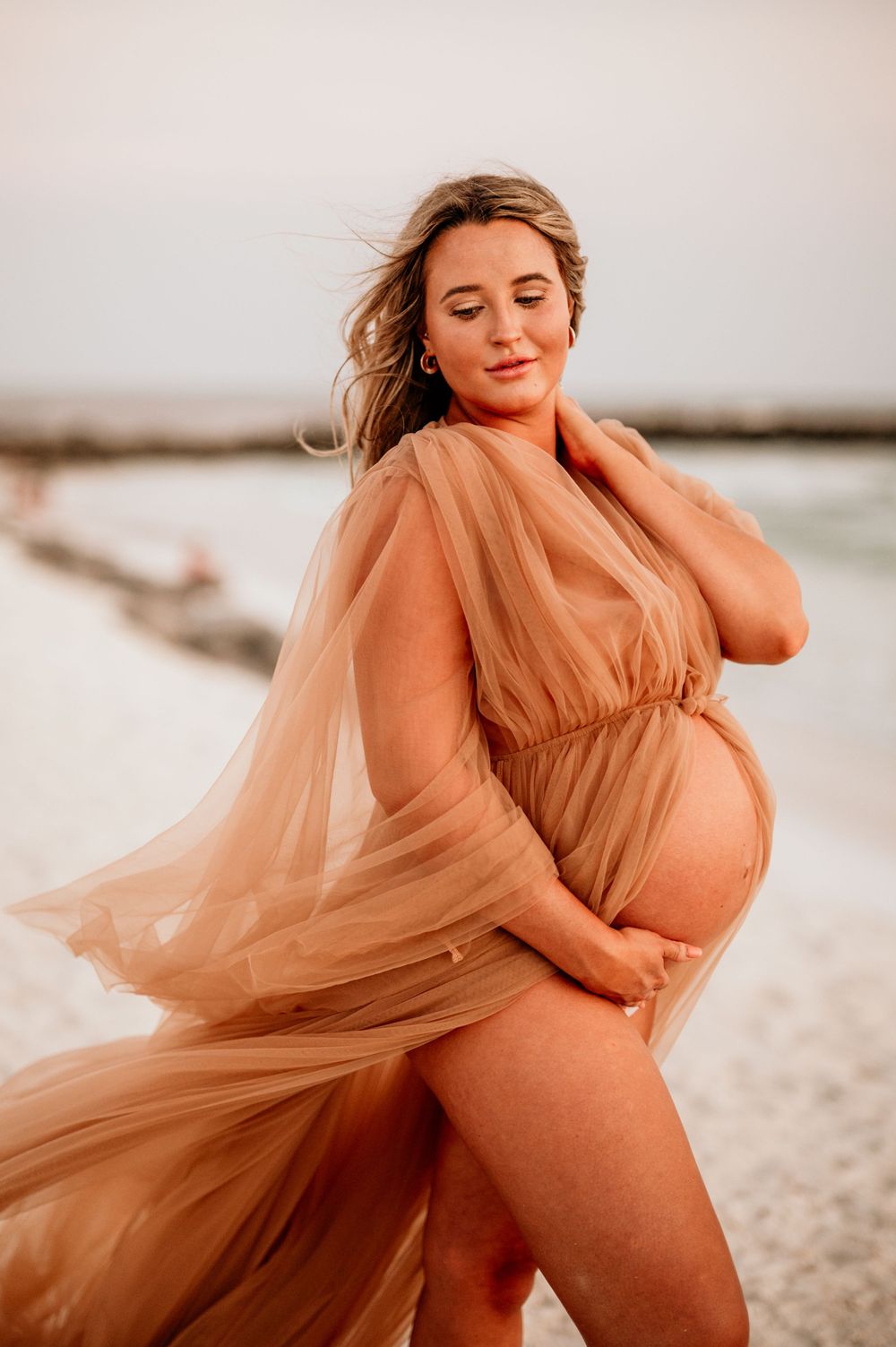 Peaceful maternity moment captured in peach dress during sunset beach photoshoot.