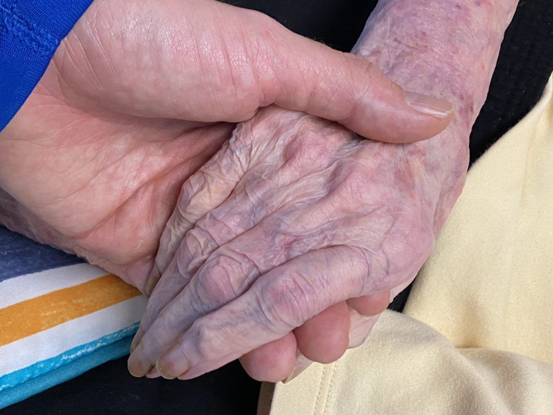 Young man's hand holds elderly woman's hand. Close up image.