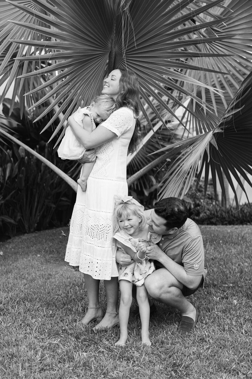 Riviera Nayarit family photographer, black and white family portrait under a large palm frond in a tropical garden setting.