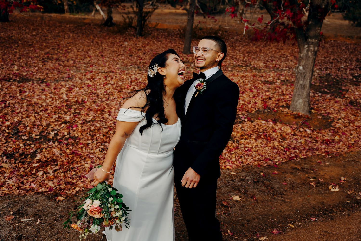 Joyful wedding moment captured under red autumn trees.