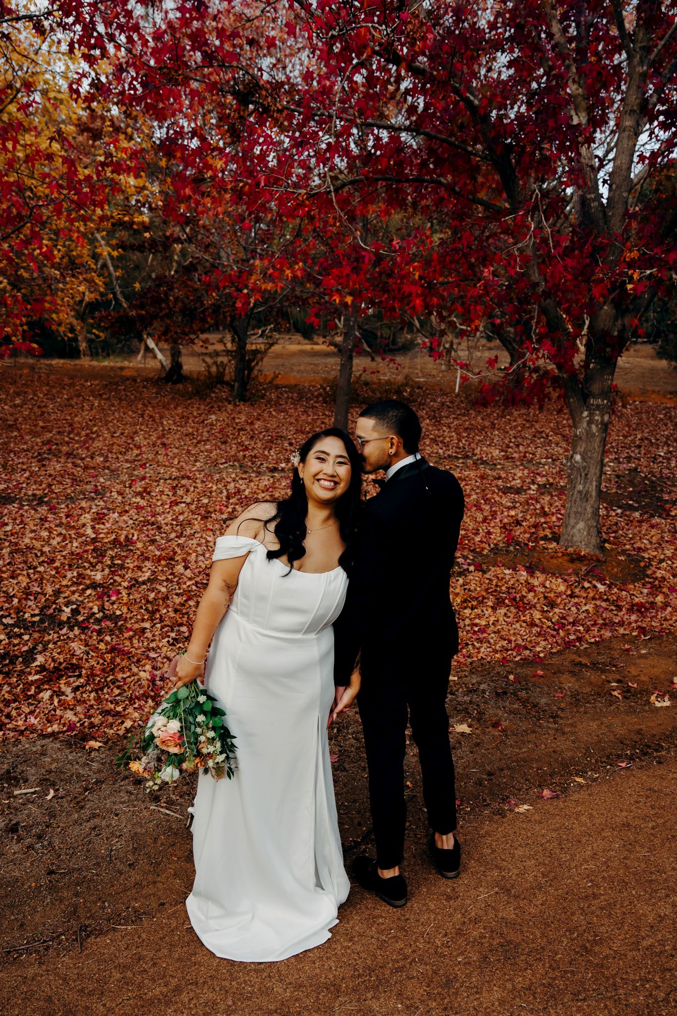 Elegant wedding photo under crimson maple trees with autumn foliage.