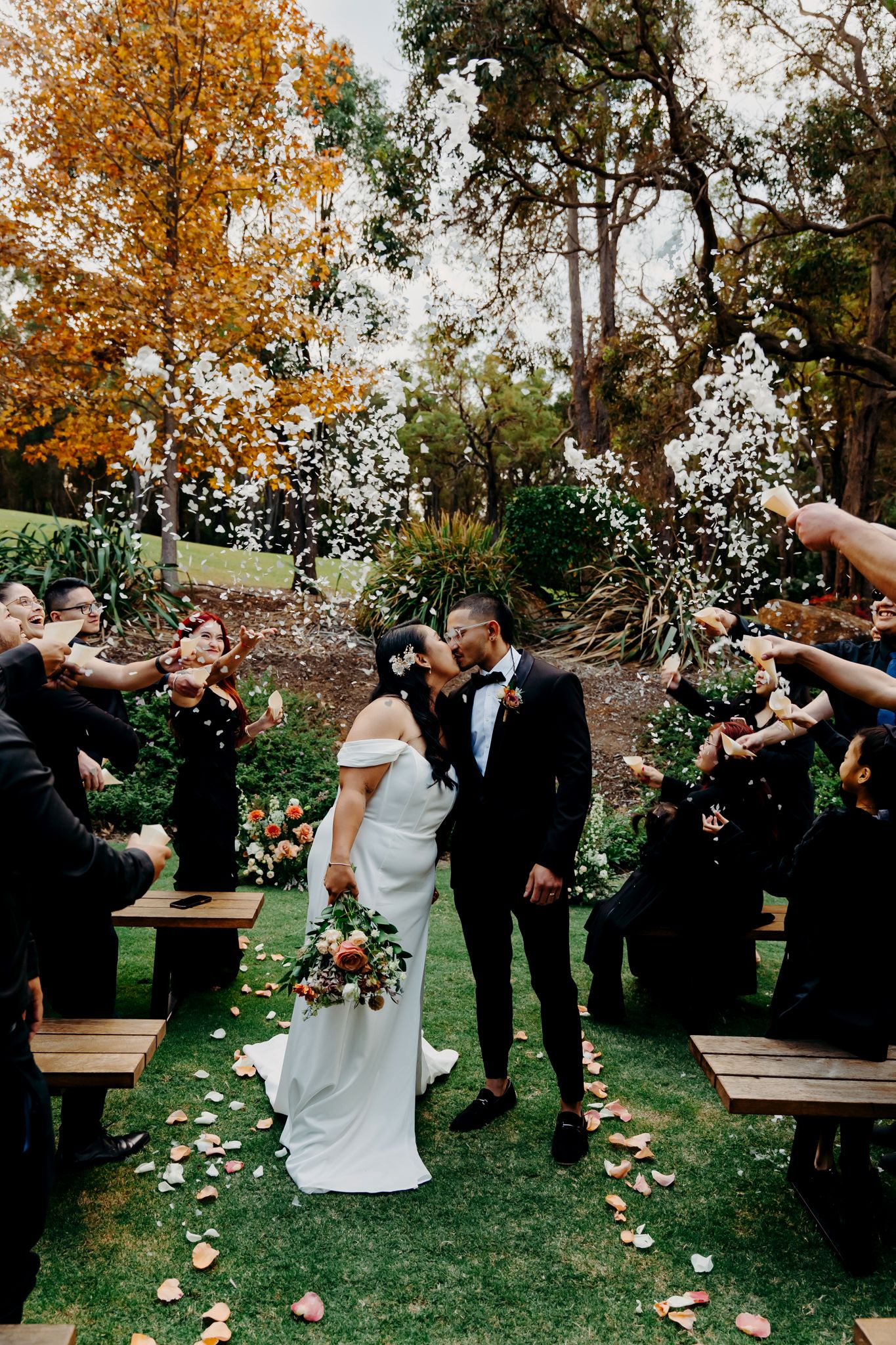 Wedding celebration with guests throwing confetti in an outdoor garden ceremony.