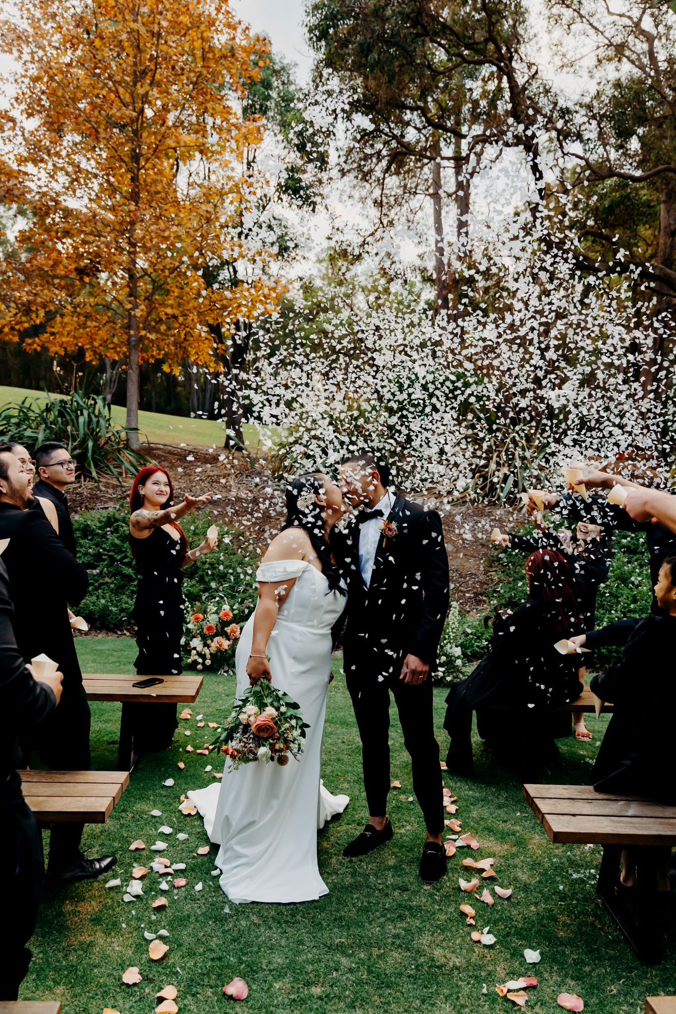 Guests shower newlyweds with white confetti during outdoor garden ceremony.