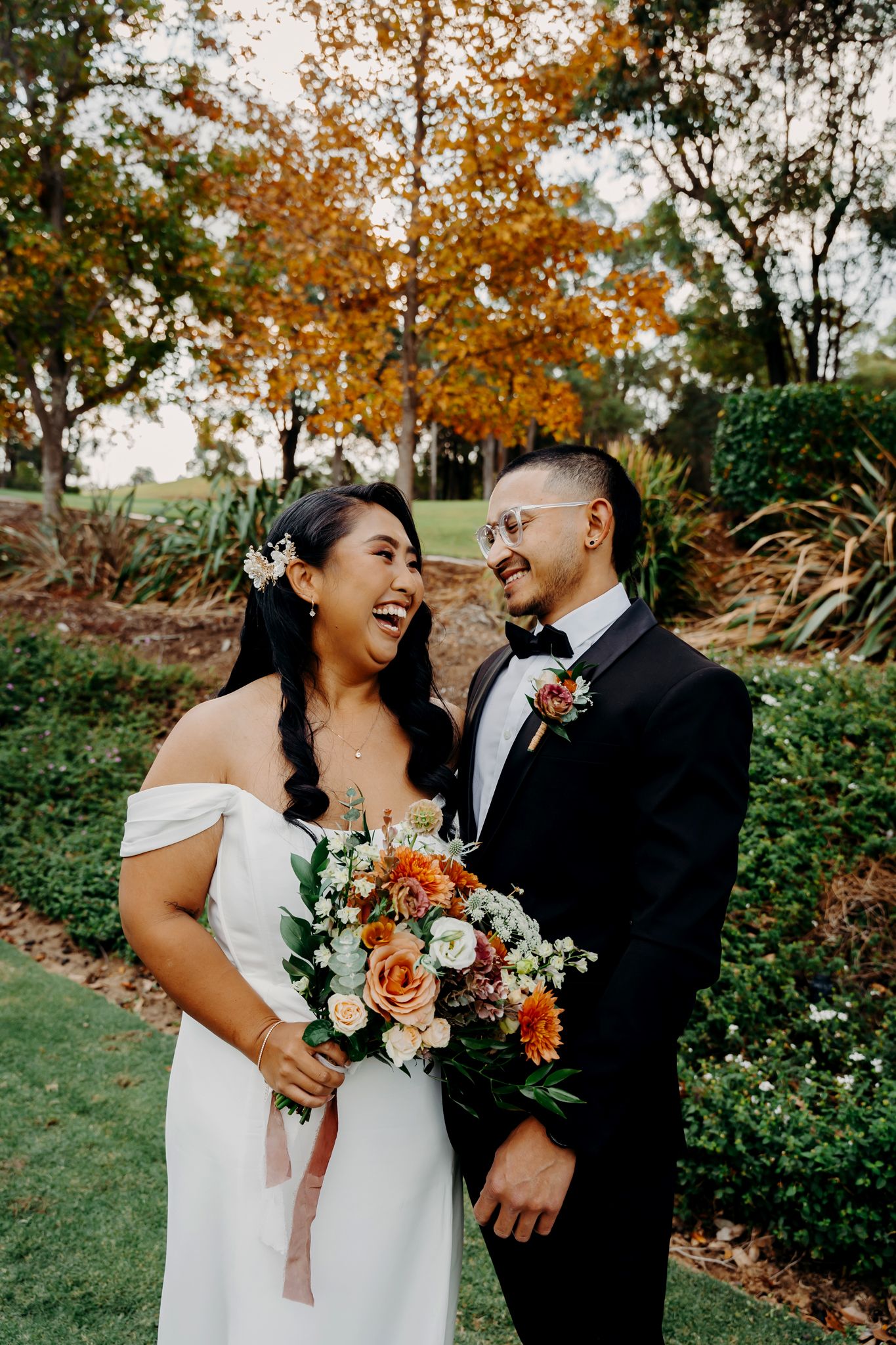 Joyful wedding couple sharing a laugh while holding an autumn-themed bouquet.