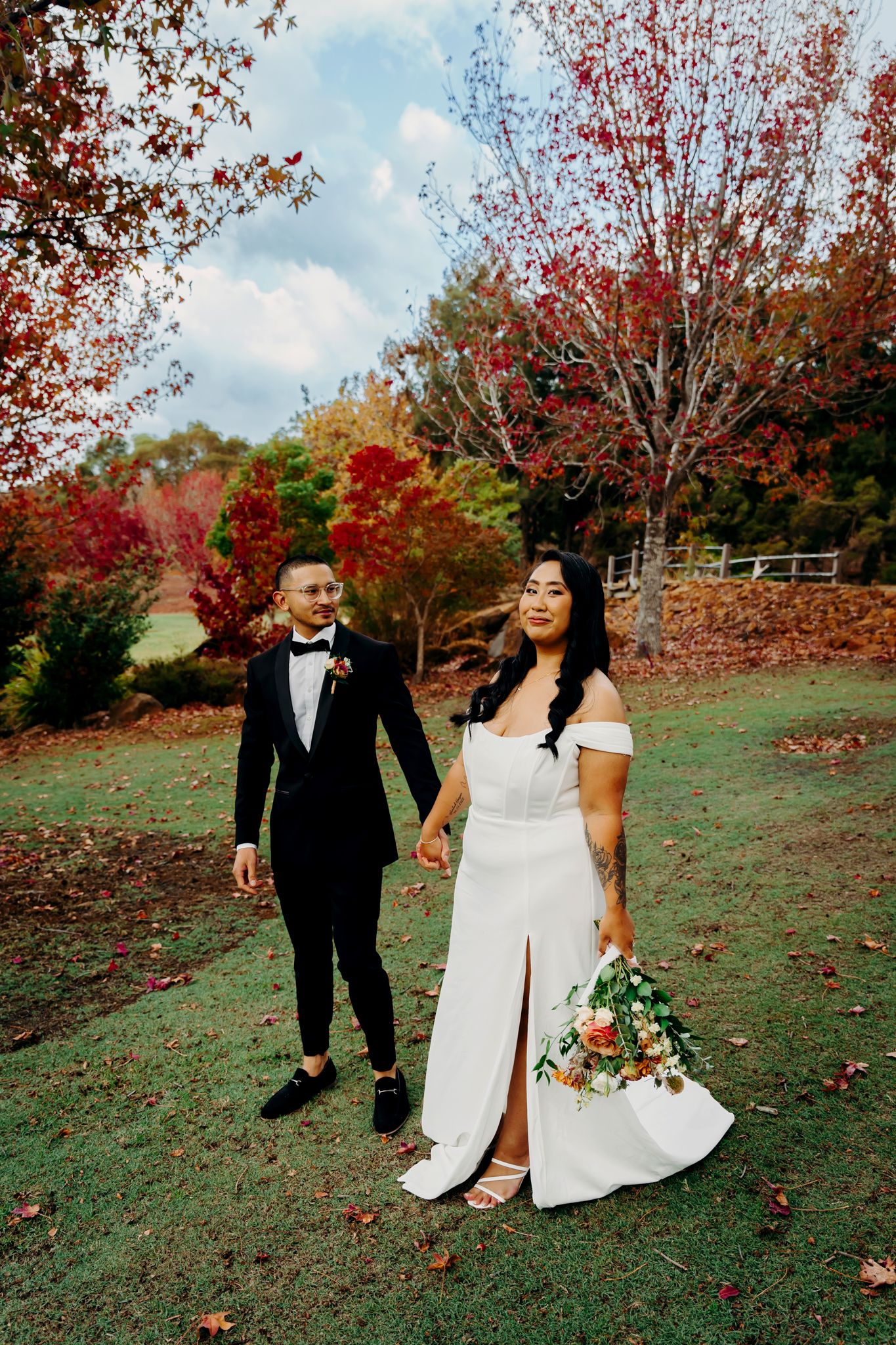 Elegant wedding couple walking through a garden with brilliant red and orange fall foliage.