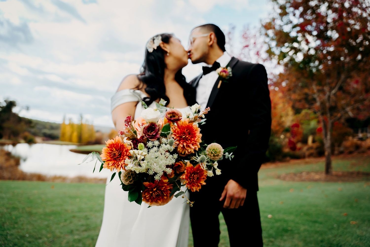 Wedding couple sharing an intimate moment against a scenic autumn backdrop with vibrant red bouquet.