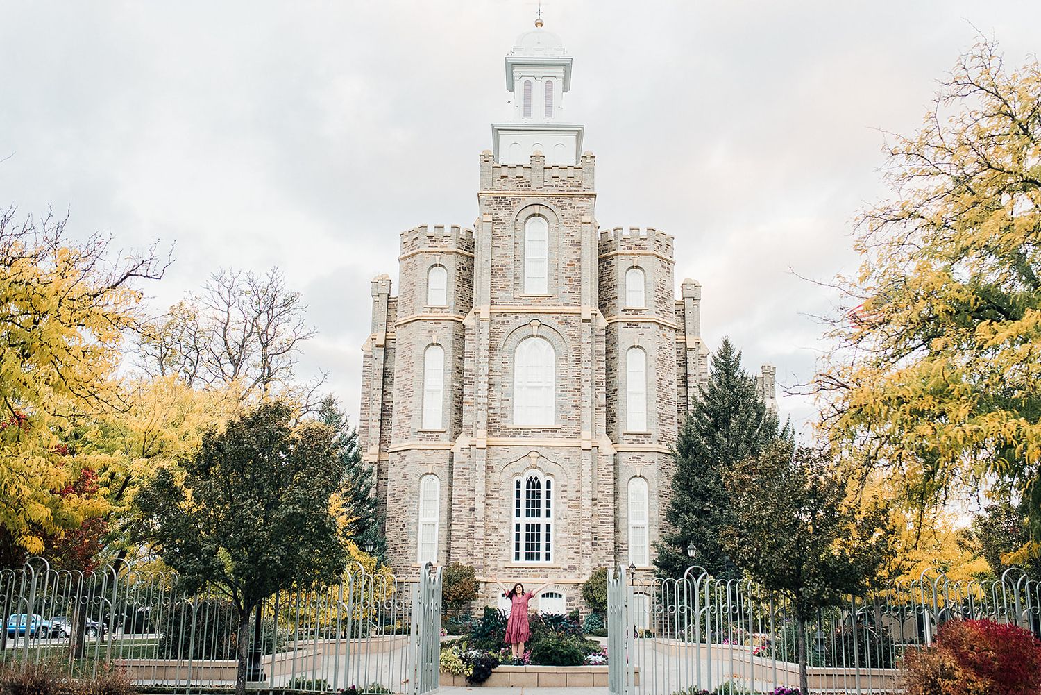 Logan Utah Temple with autumn trees and ornate architecture against cloudy sky.