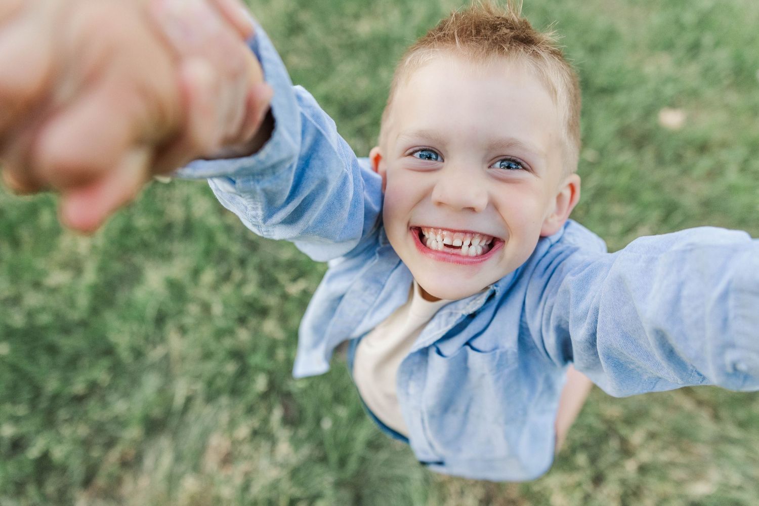 Excited young boy with blue eyes spinning and laughing while holding an adults hand outdoors.