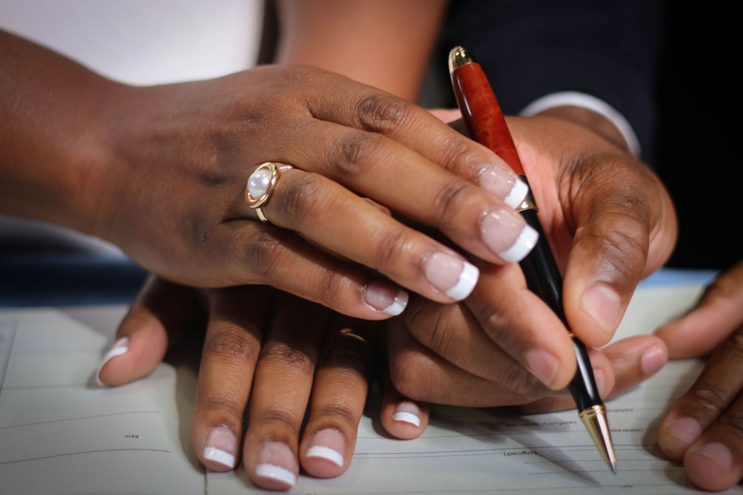 Close-up of hands holding a pen showing an engagement ring with French manicured nails.