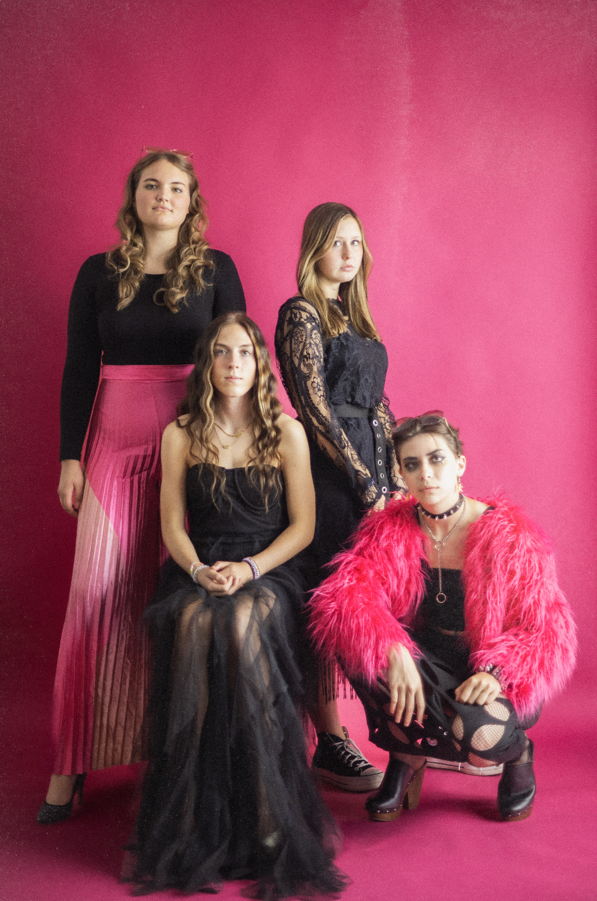 Three people in black attire pose against a vibrant pink backdrop with a bright pink feathered accessory.