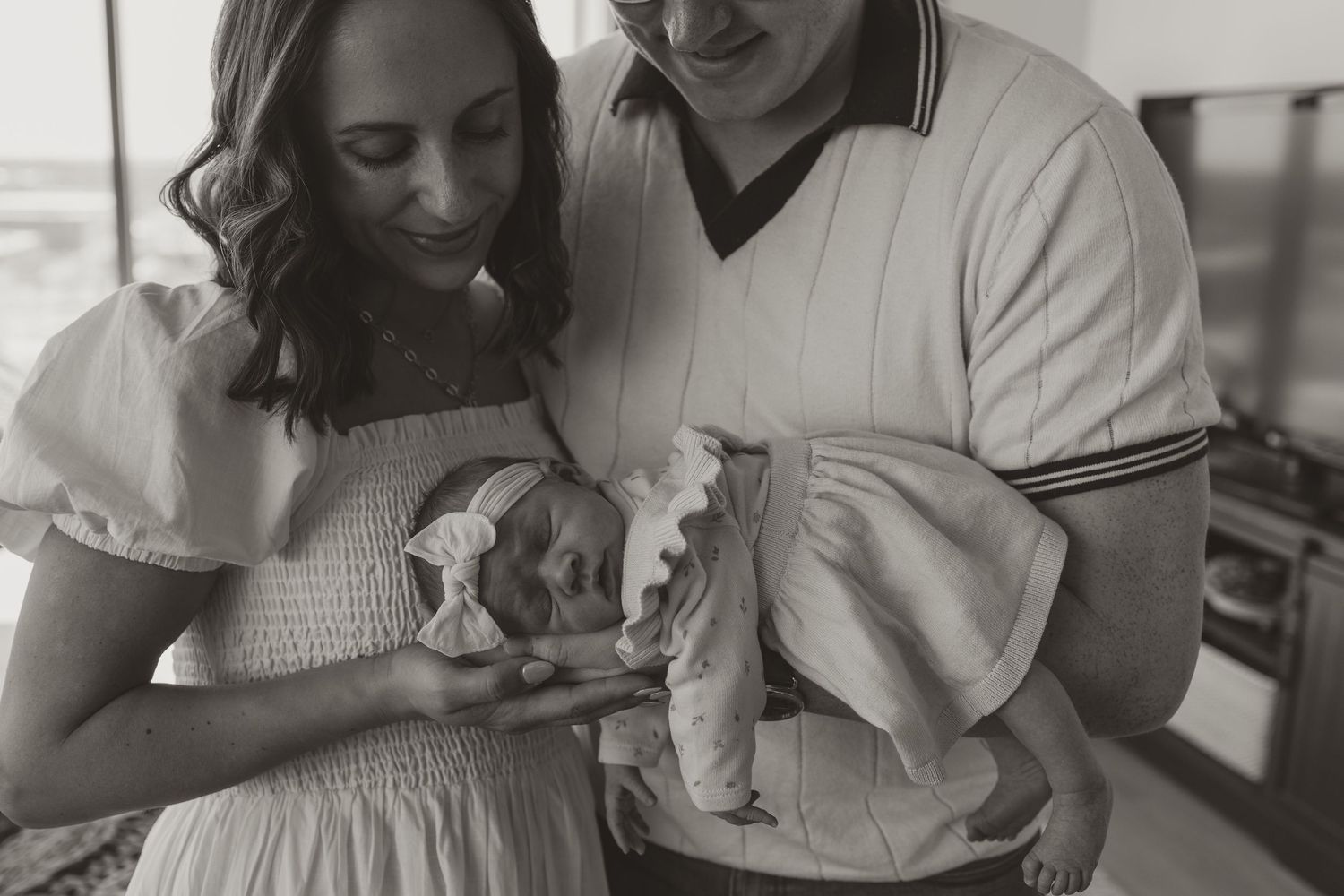 Black and white photo of couple holding newborn baby in a tender moment at home.