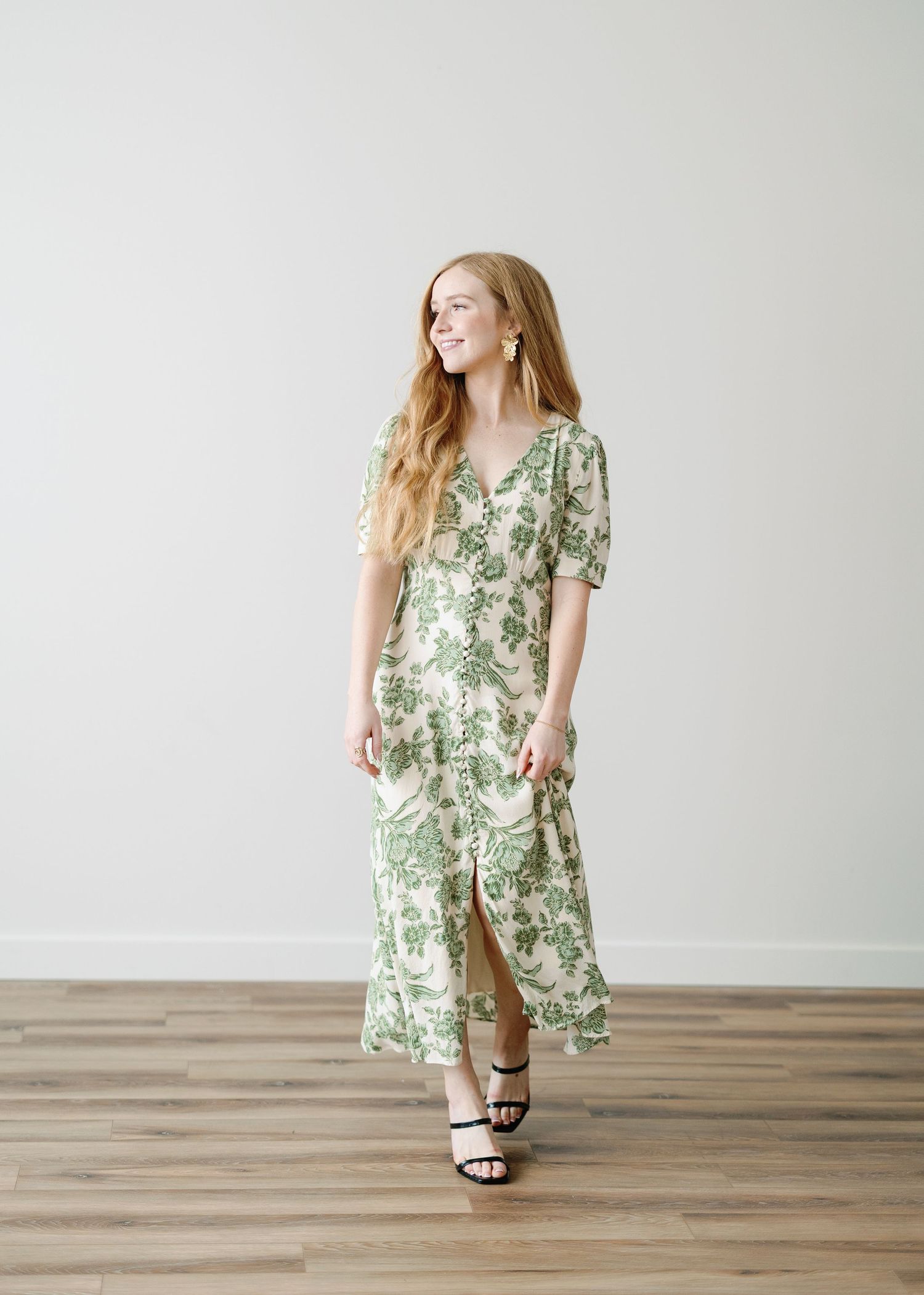 A photographer in a mint green dress holds camera equipment while standing in a sunlit grassy field at golden hour.