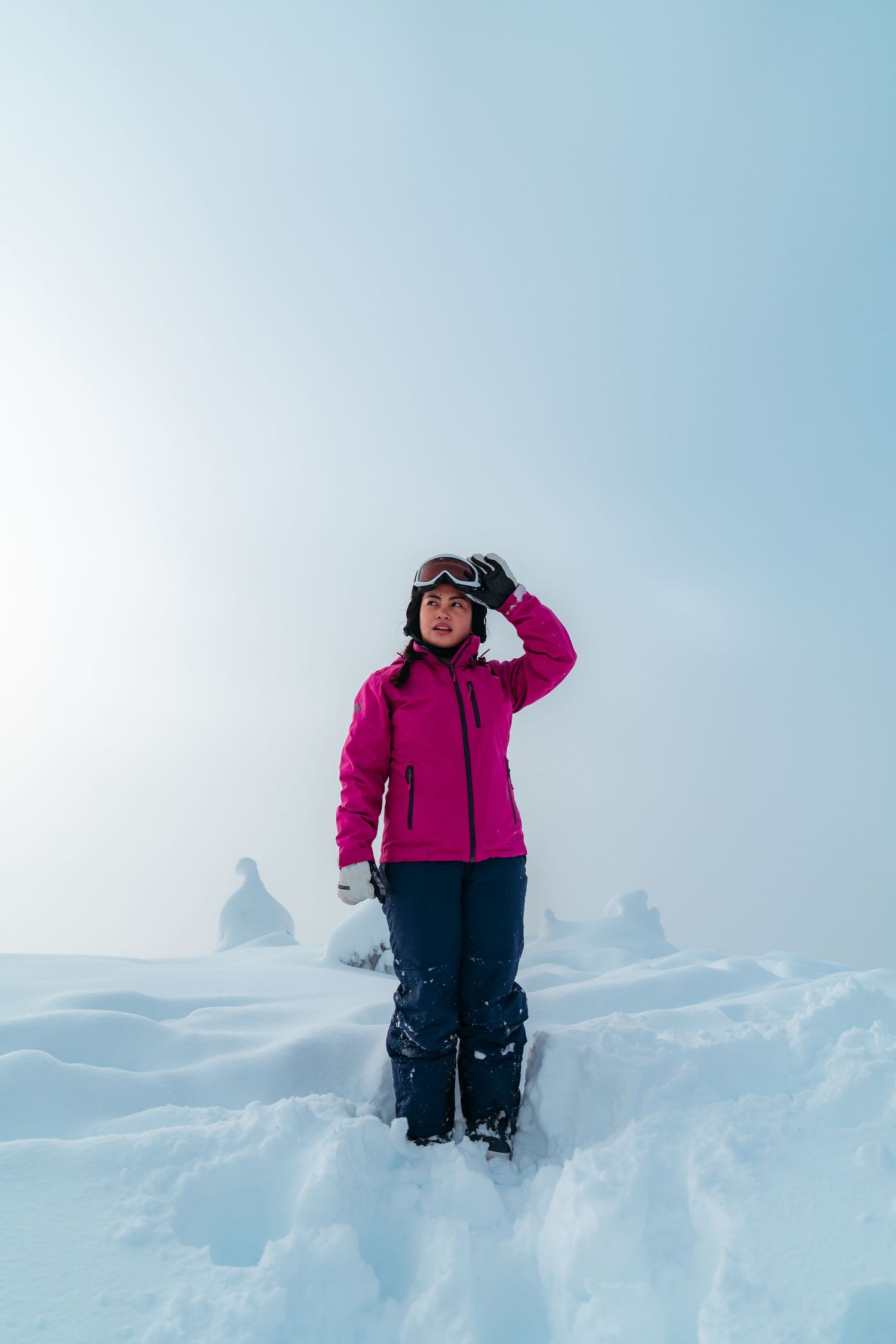 Winter adventurer in bright pink jacket standing in deep snow with mountains in background.