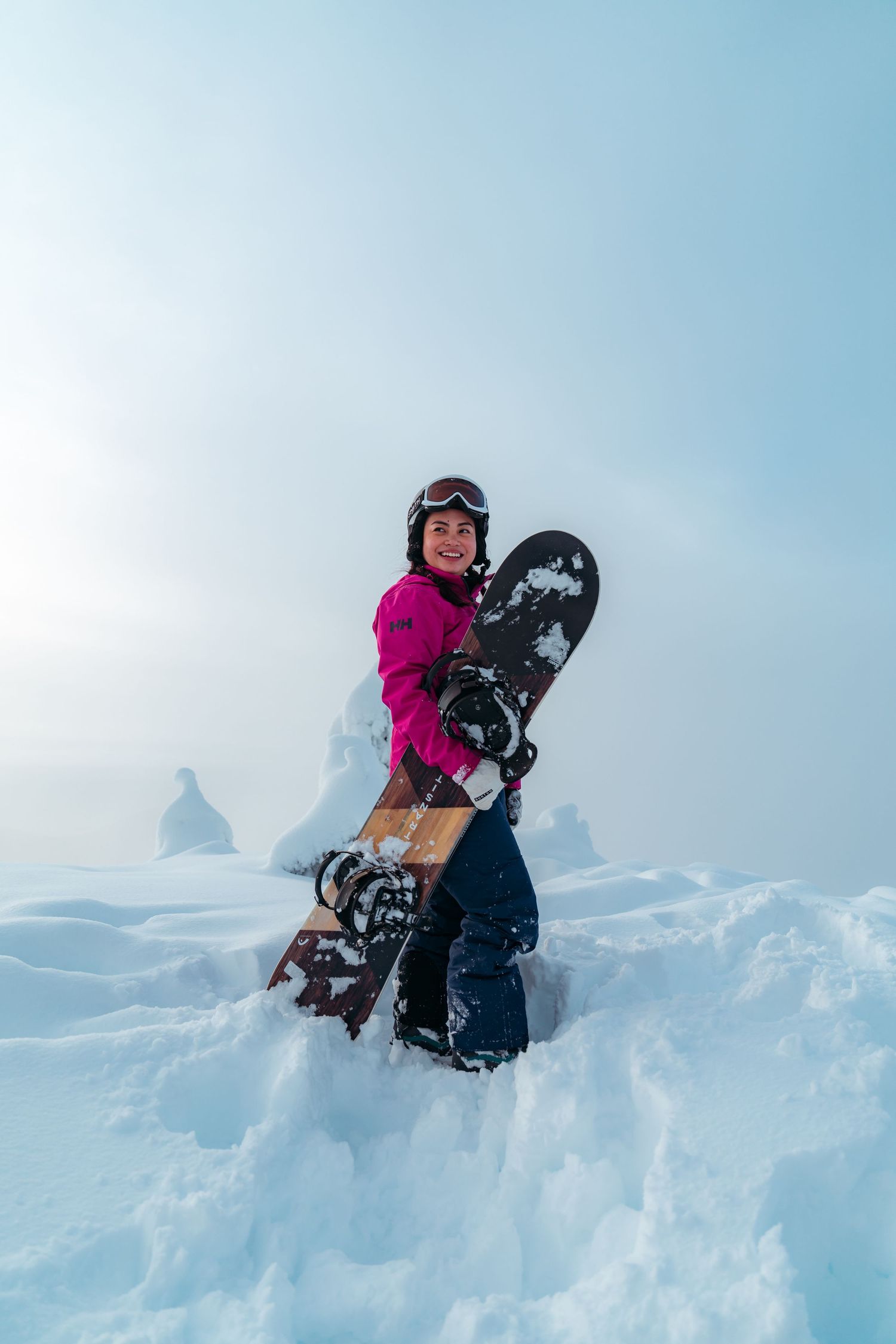 Snowboarder in bright pink jacket holding board while standing in deep snow.