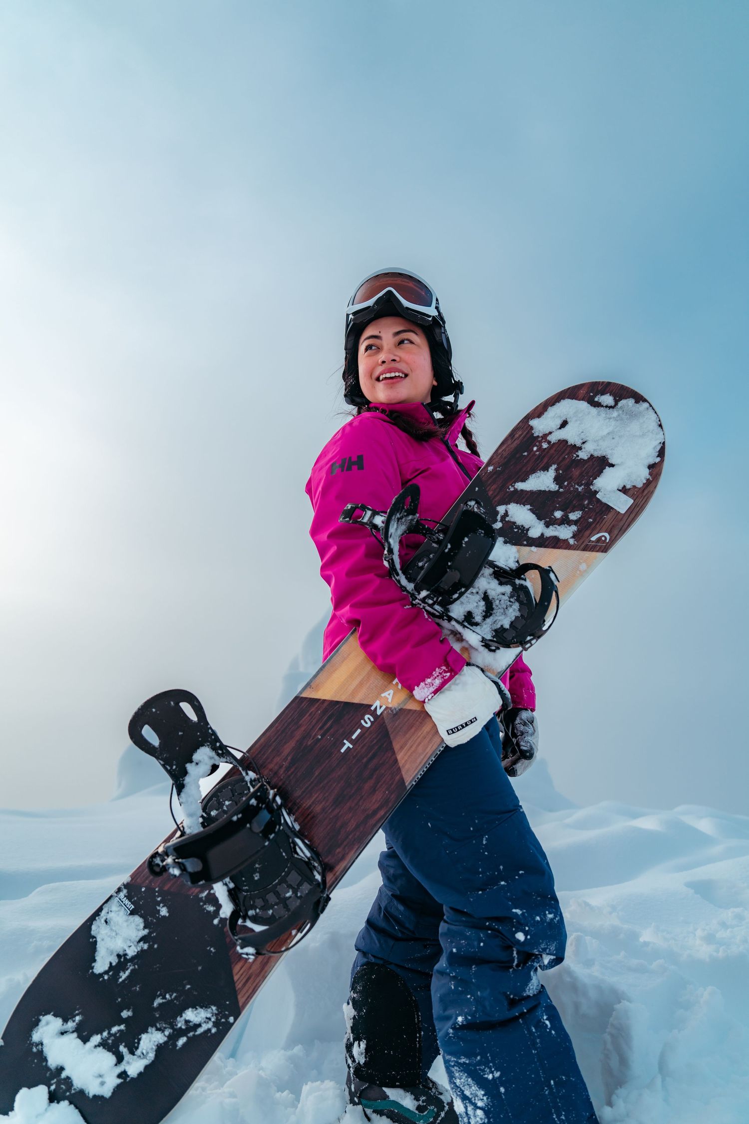 Snowboarder in pink jacket holding snowboard while standing in snowy terrain.