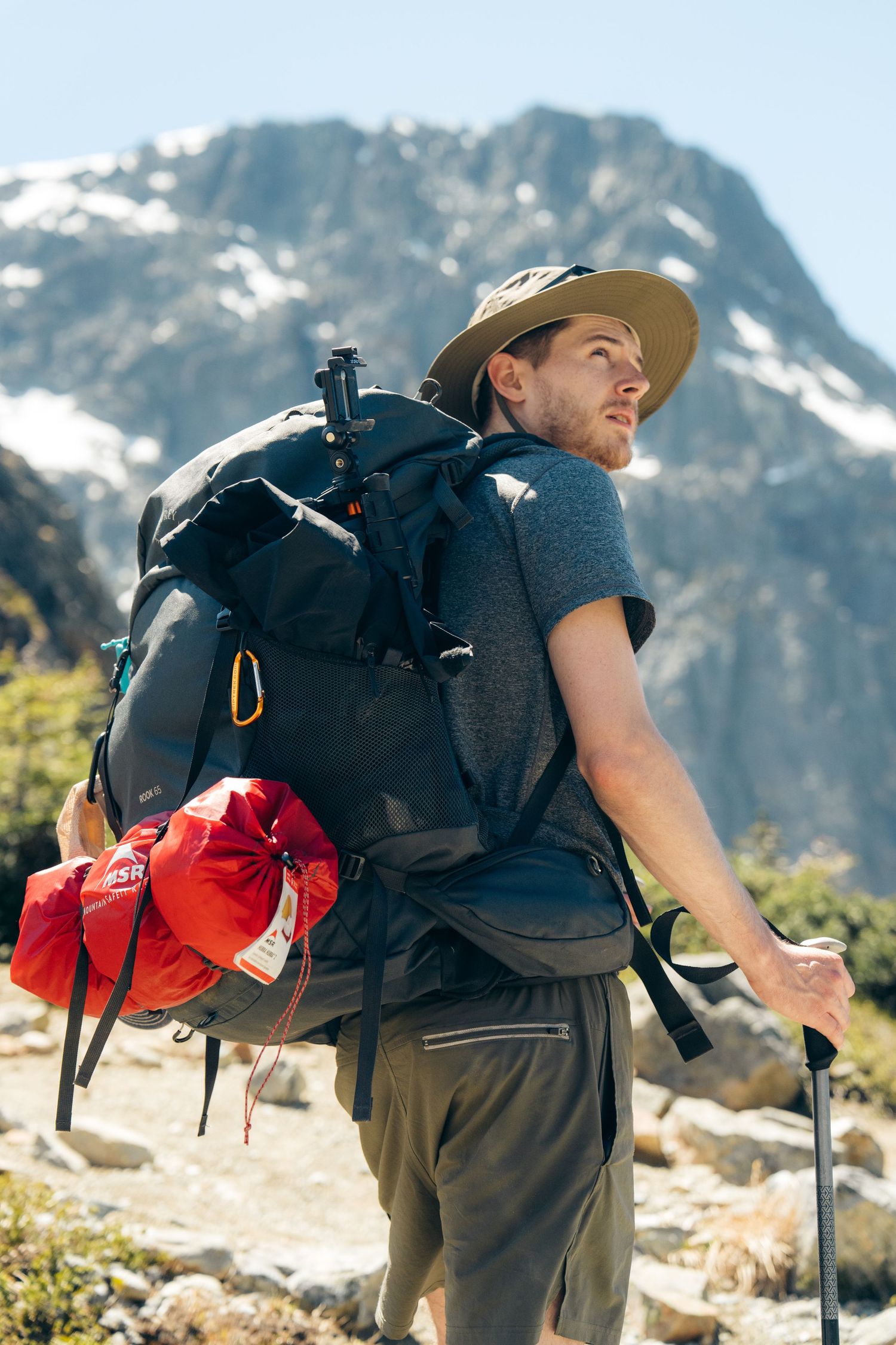 Backpacker with large pack and hiking poles gazes up at mountain peaks.