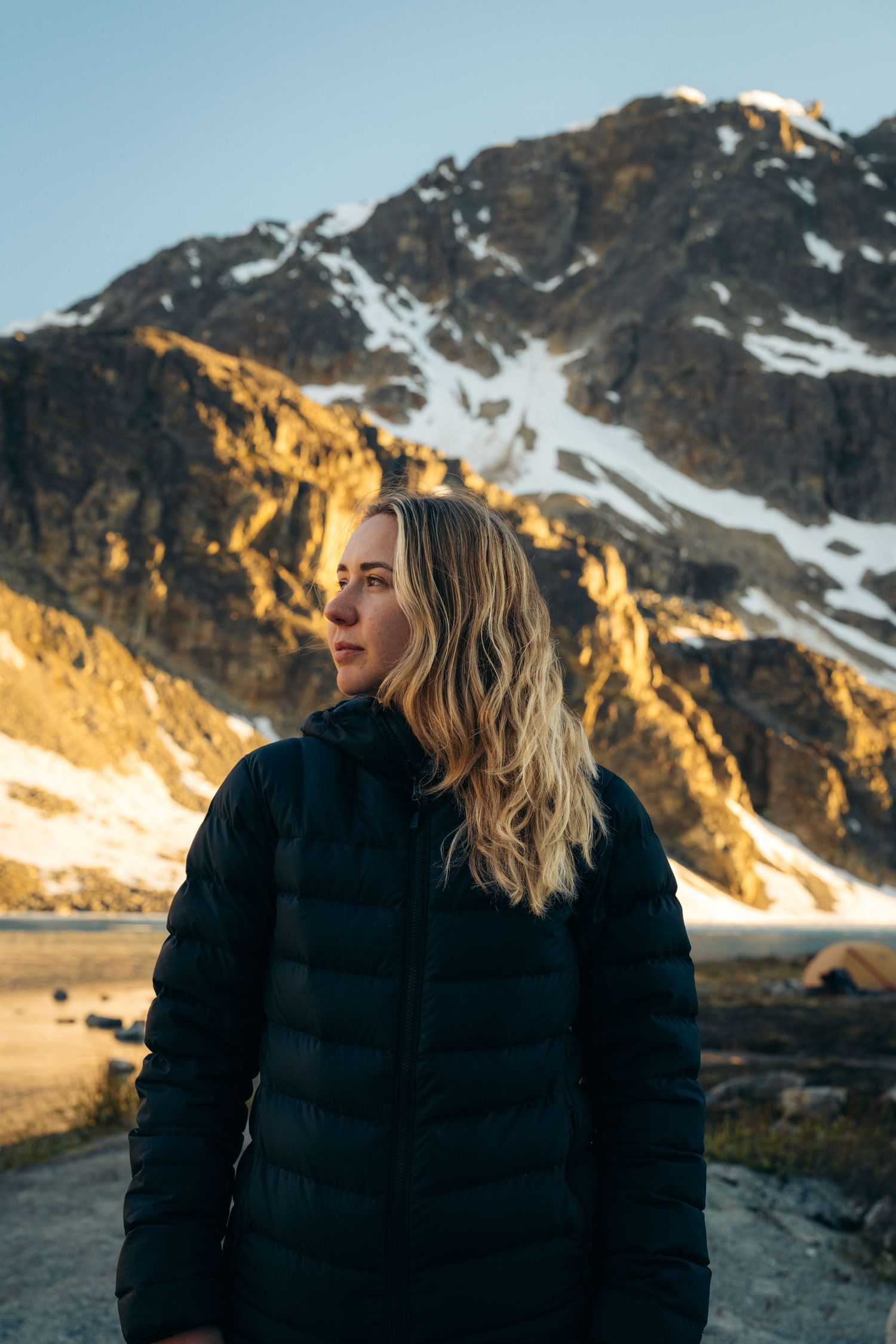 Person in black puffy jacket against golden mountain landscape at sunset.