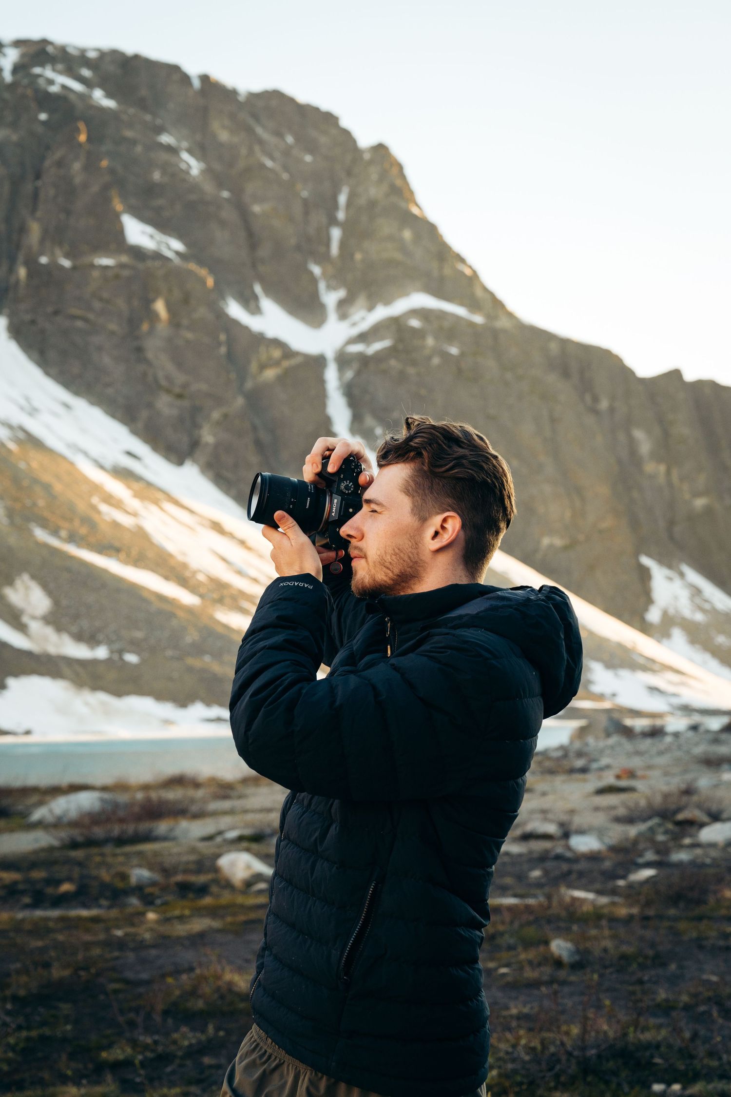 Photographer in dark hoodie captures images of mountain scenery.