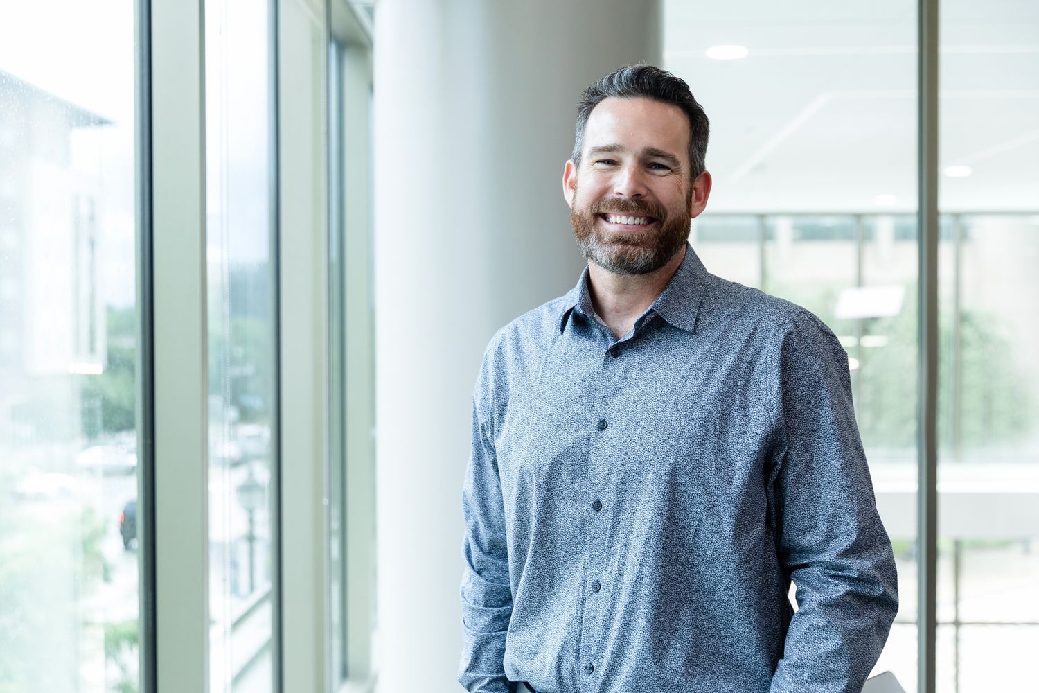 Man standing inside Utah state university getting his headshot while he smiles. While standing in the Jon M. Huntsman building.