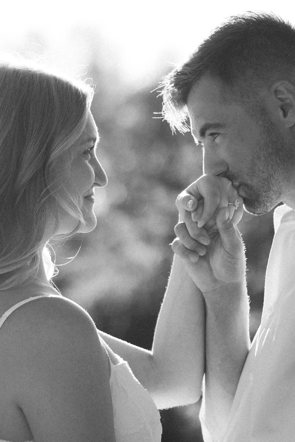 Romantic black and white close-up of bearded man gently kissing womans hand while gazing at her lovingly.