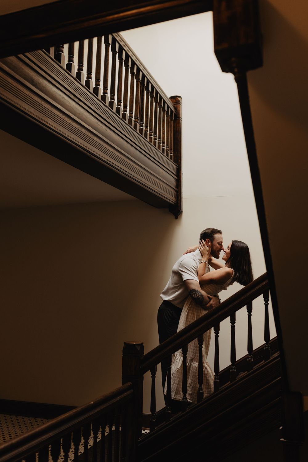 Couple kissing on a wooden staircase landing in a warmly lit interior.