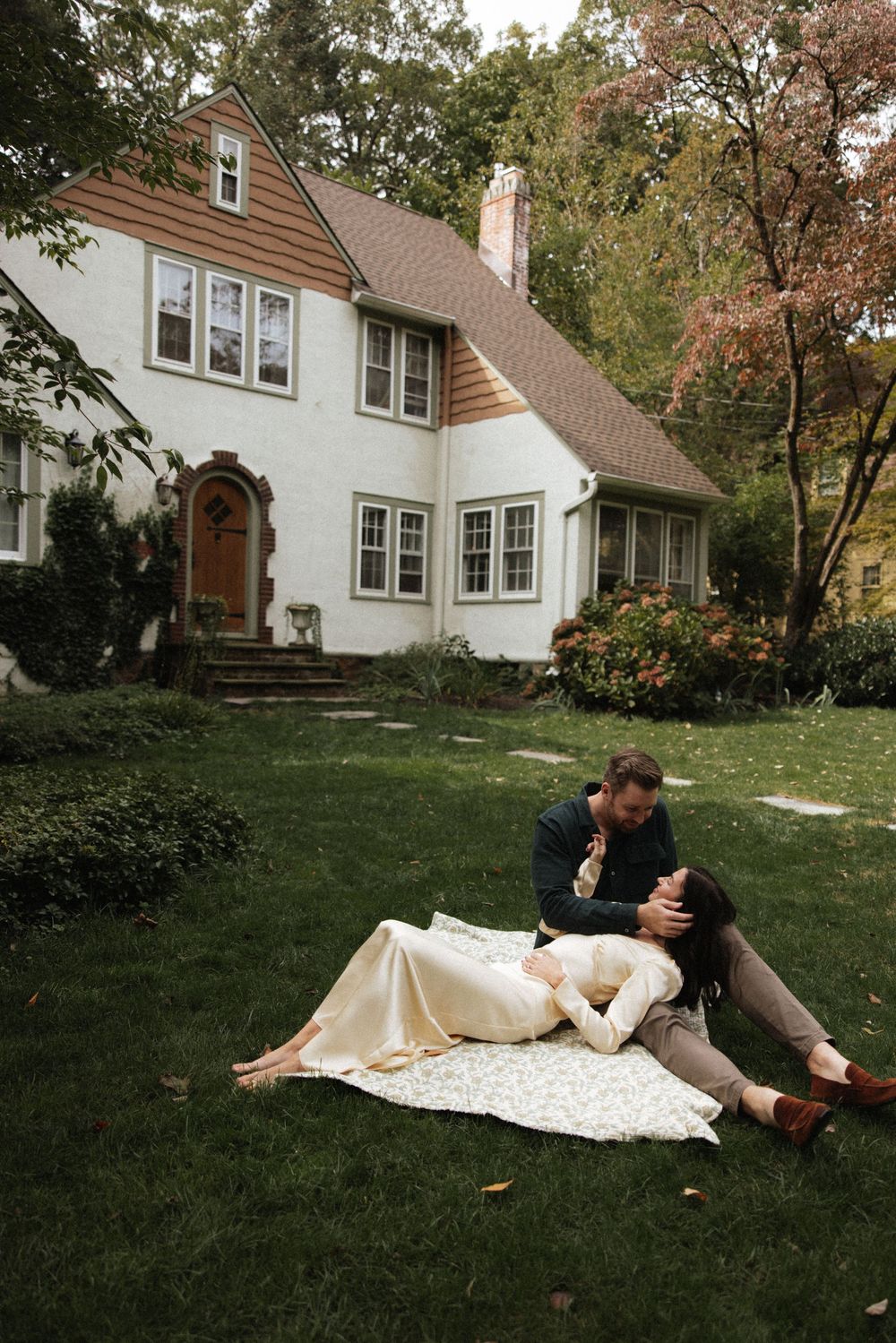 Couple relaxing on a blanket in front of a charming white stucco house surrounded by lush autumn garden.