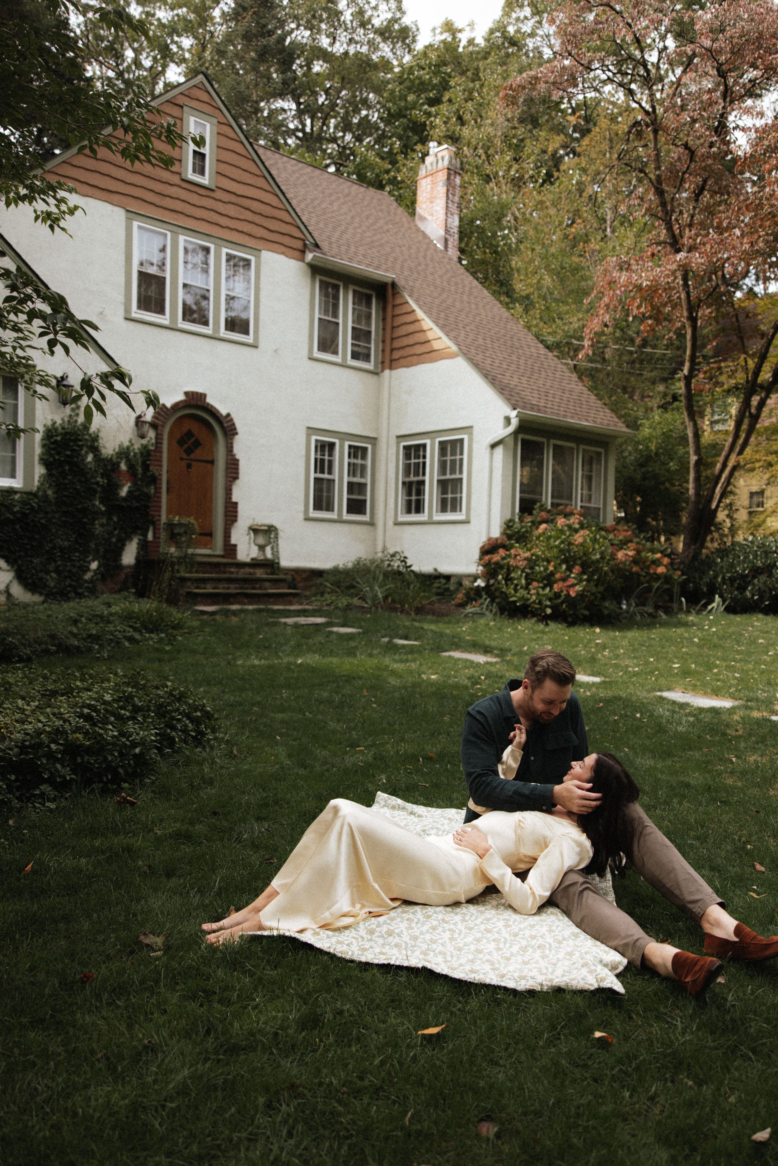 Couple relaxing on a blanket in front of a charming white stucco house surrounded by lush autumn garden.