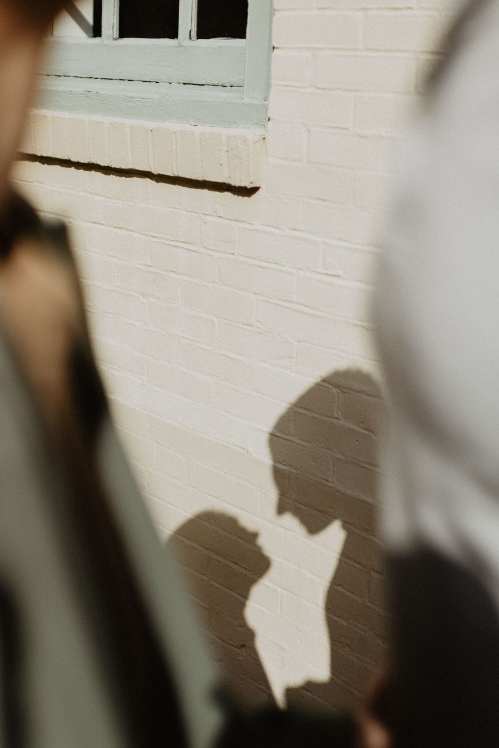 Romantic shadow silhouette of a couple about to kiss cast on a white brick wall in sunlight.