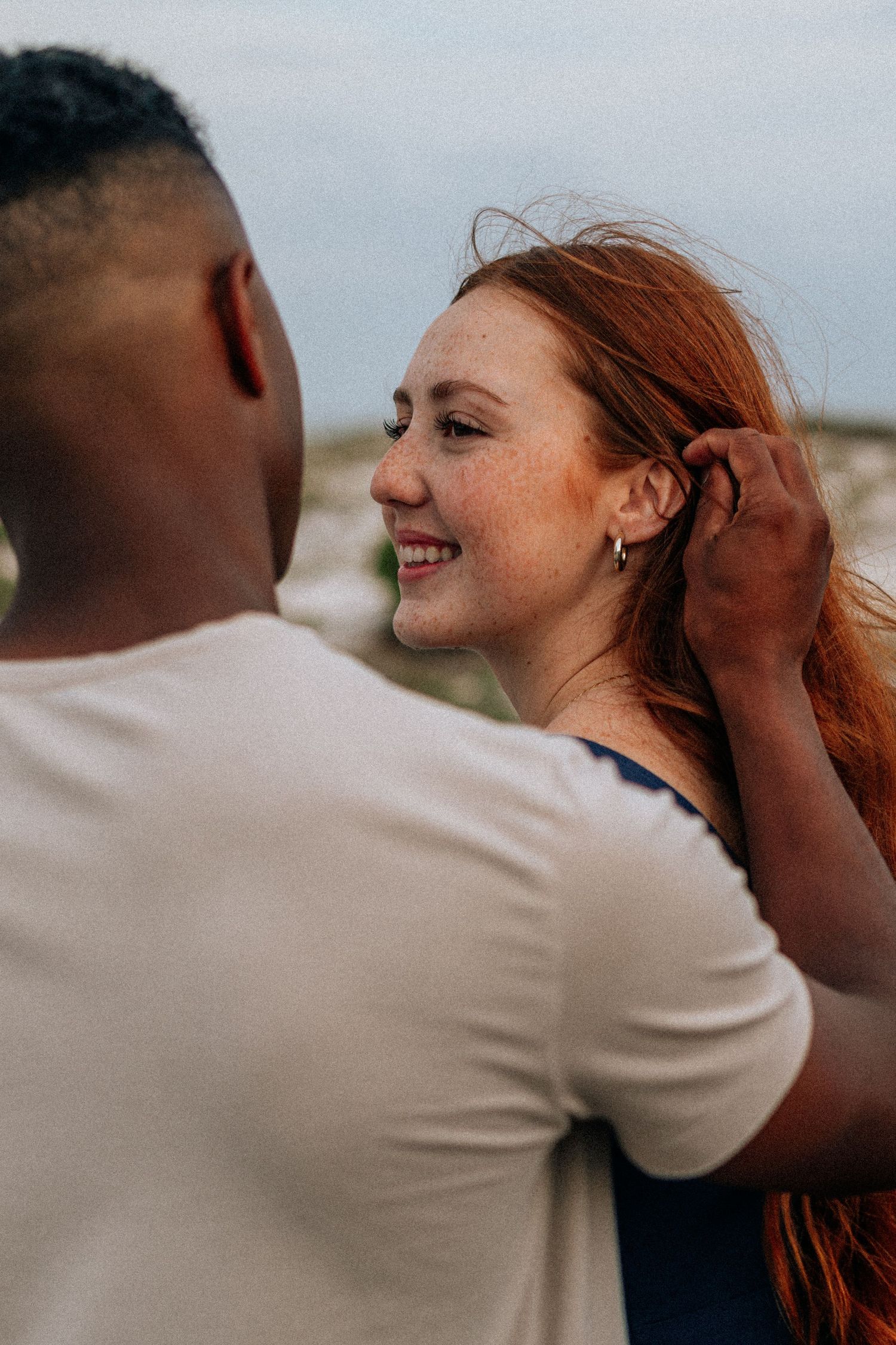 Intimate moment between a couple outdoors as he gently tucks her red hair behind her ear.