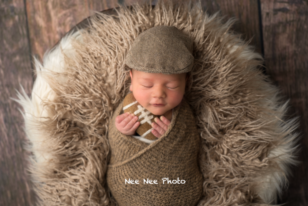 Newborn baby sleeping peacefully in a fluffy brown nest, wrapped in knit swaddle and wearing a newsboy cap. Embracing Life’s Beauty