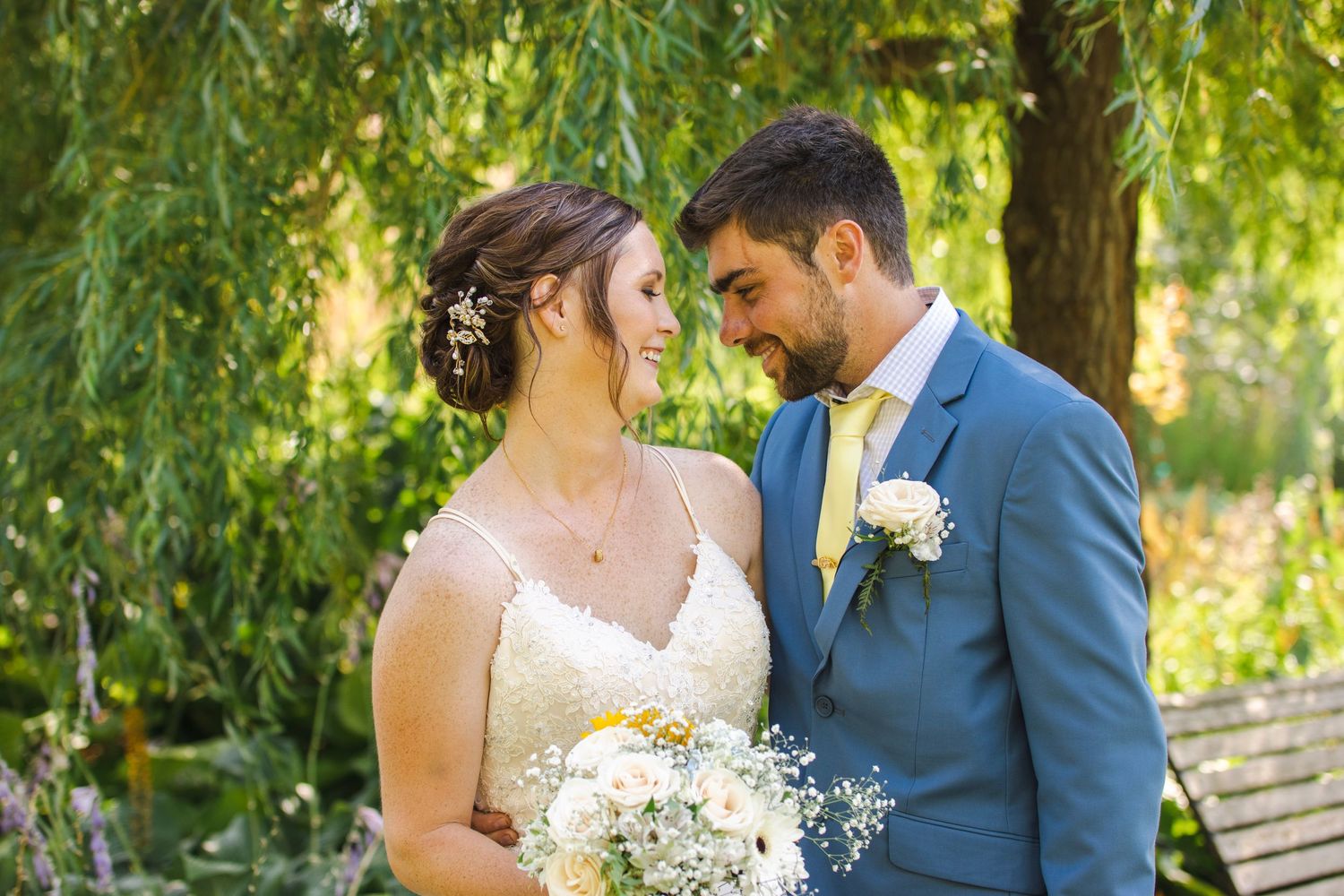 Wedding couple sharing an intimate moment under a drooping willow tree with white floral bouquet.