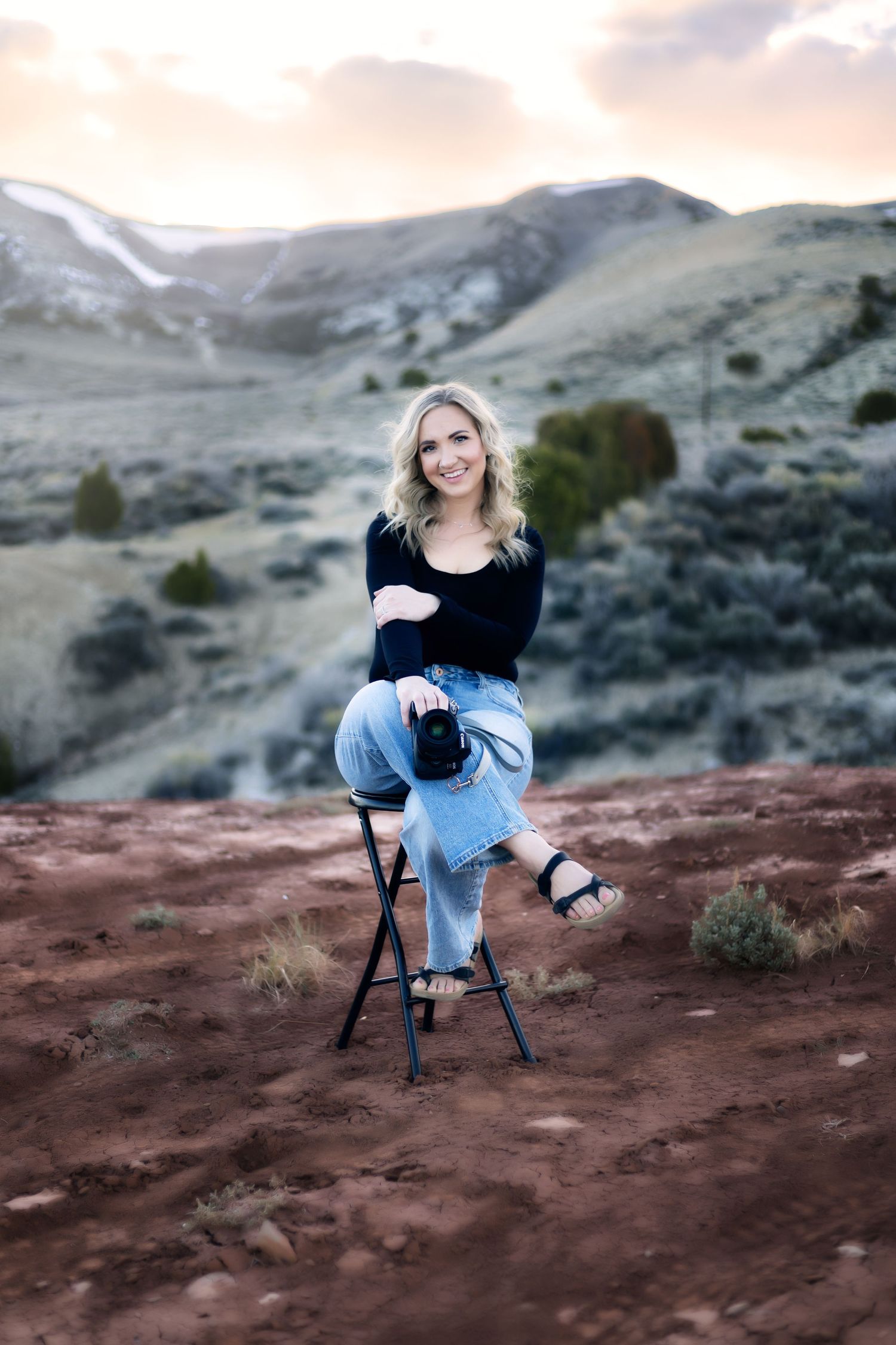 Portrait of person sitting on stool against mountain backdrop with dramatic lighting.