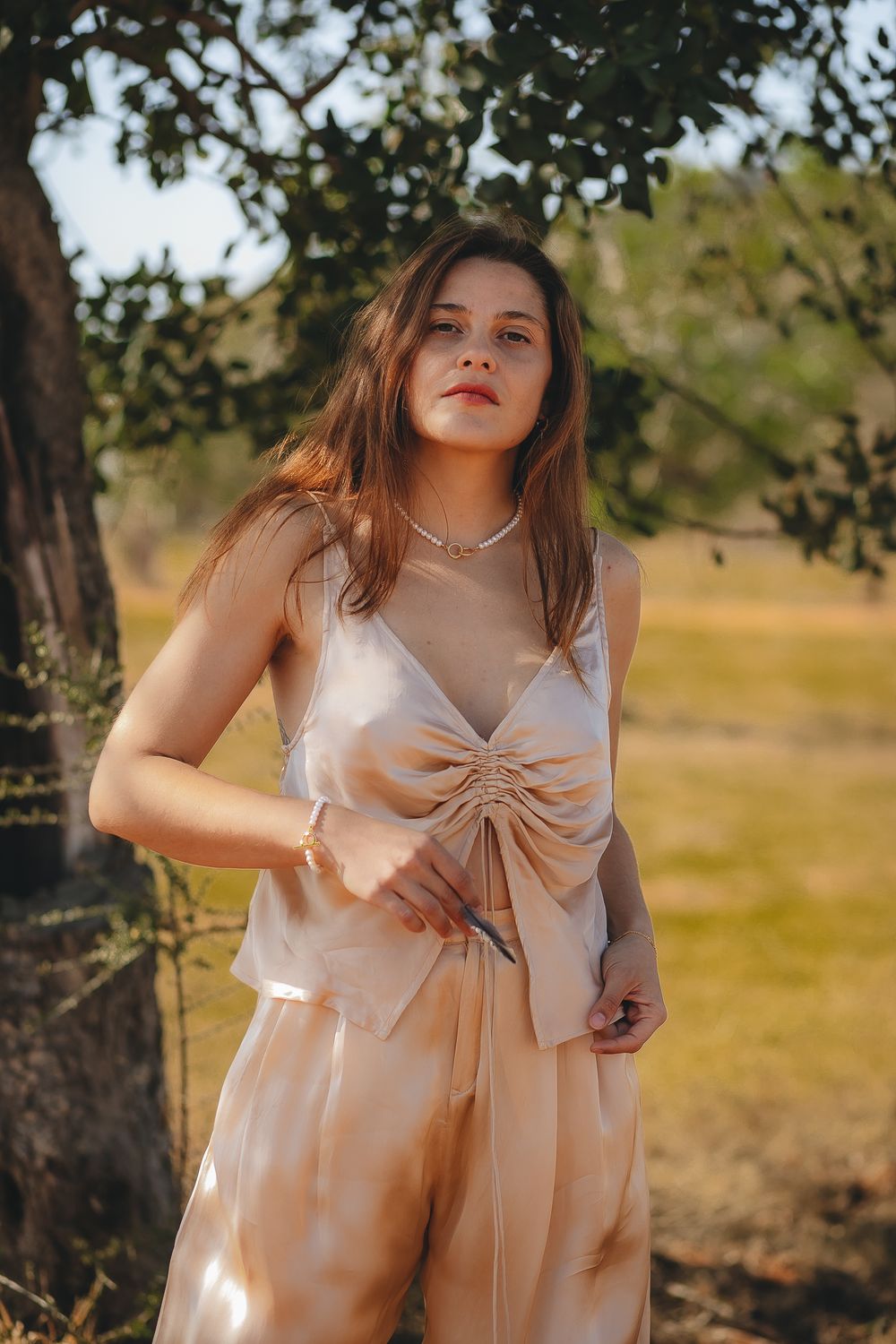 Woman wearing light beige bow dress standing in golden afternoon sunlight.