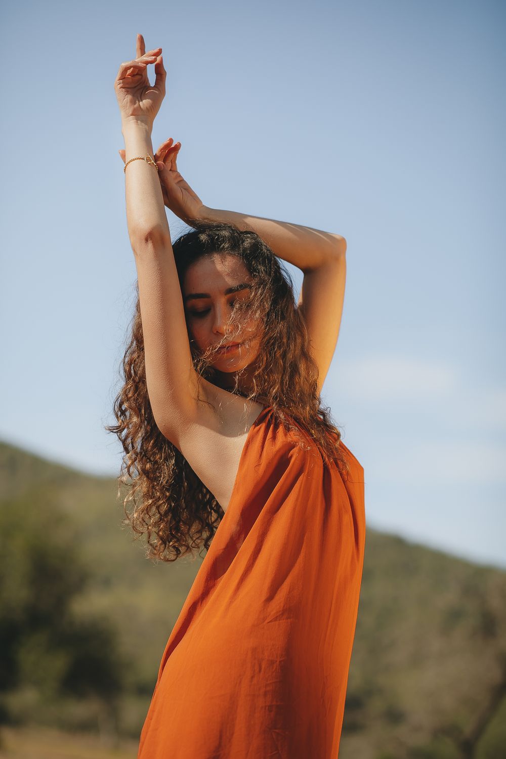 Artistic shot of a flowing orange dress in sunlight against a natural outdoor backdrop.