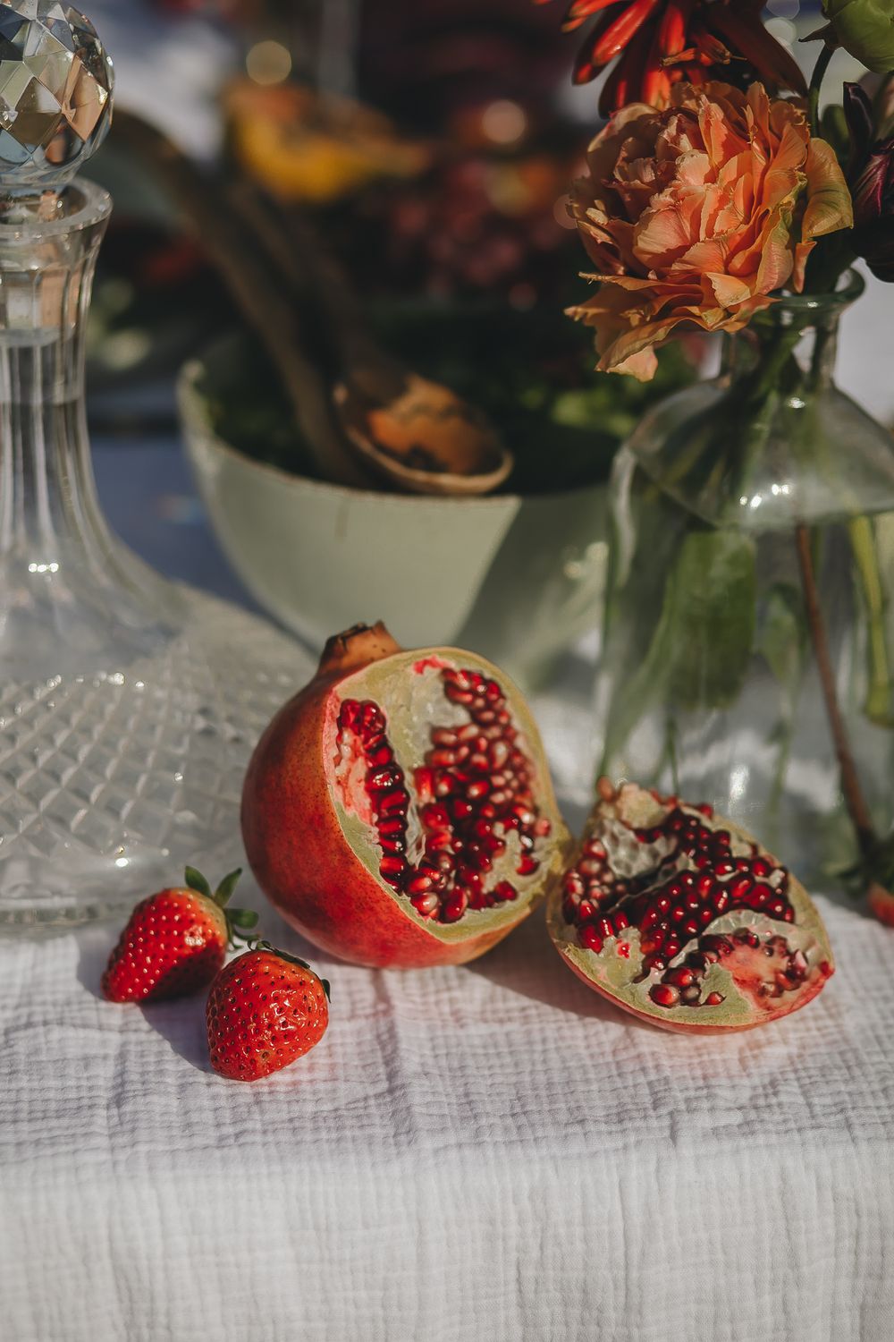 Fresh cut pomegranate and strawberries displayed with flowers in elegant table setting.