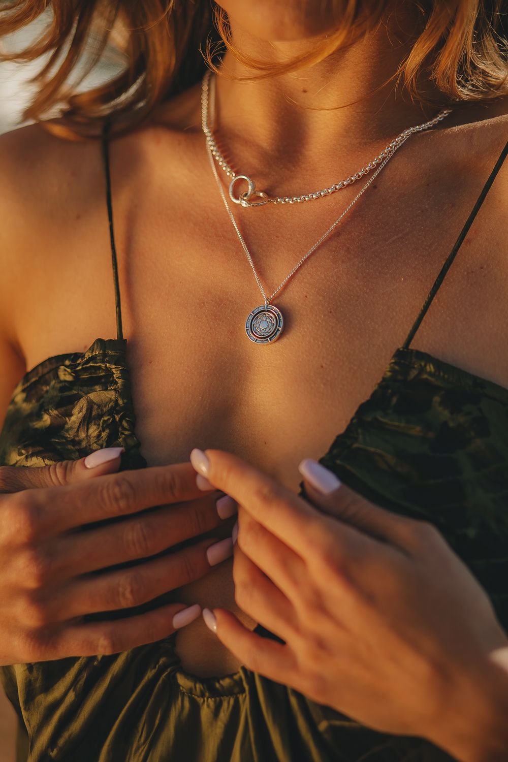 Close-up of layered gold necklaces with pendant against olive green fabric in warm lighting.