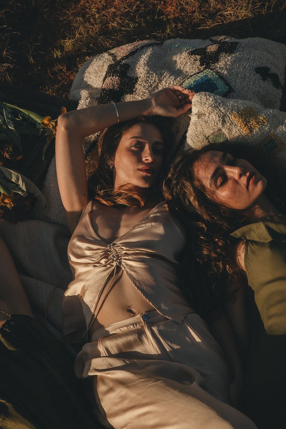 Artistic portrait of people reclining on white fabric in dappled sunlight.