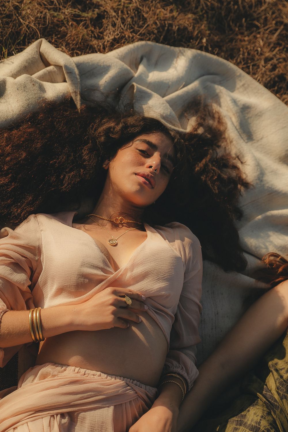 Ethereal portrait of someone lying on white fabric with curly hair splayed out in dramatic lighting.