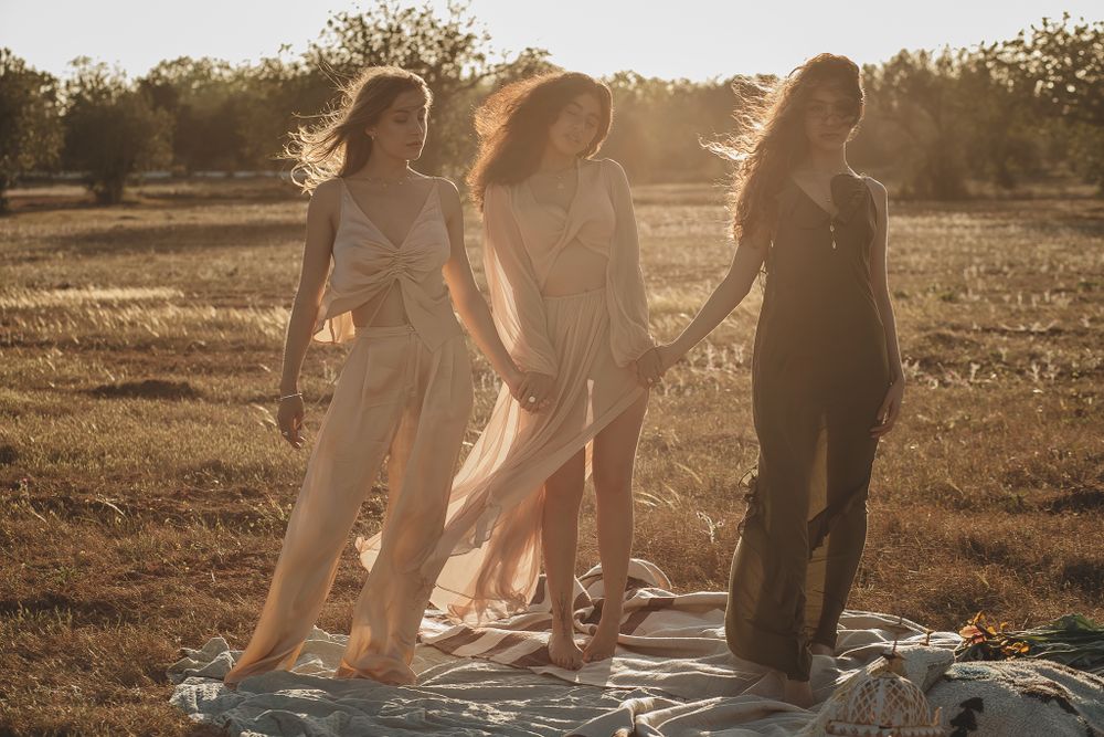 Group in flowing dresses dancing together in a sunlit field at golden hour.
