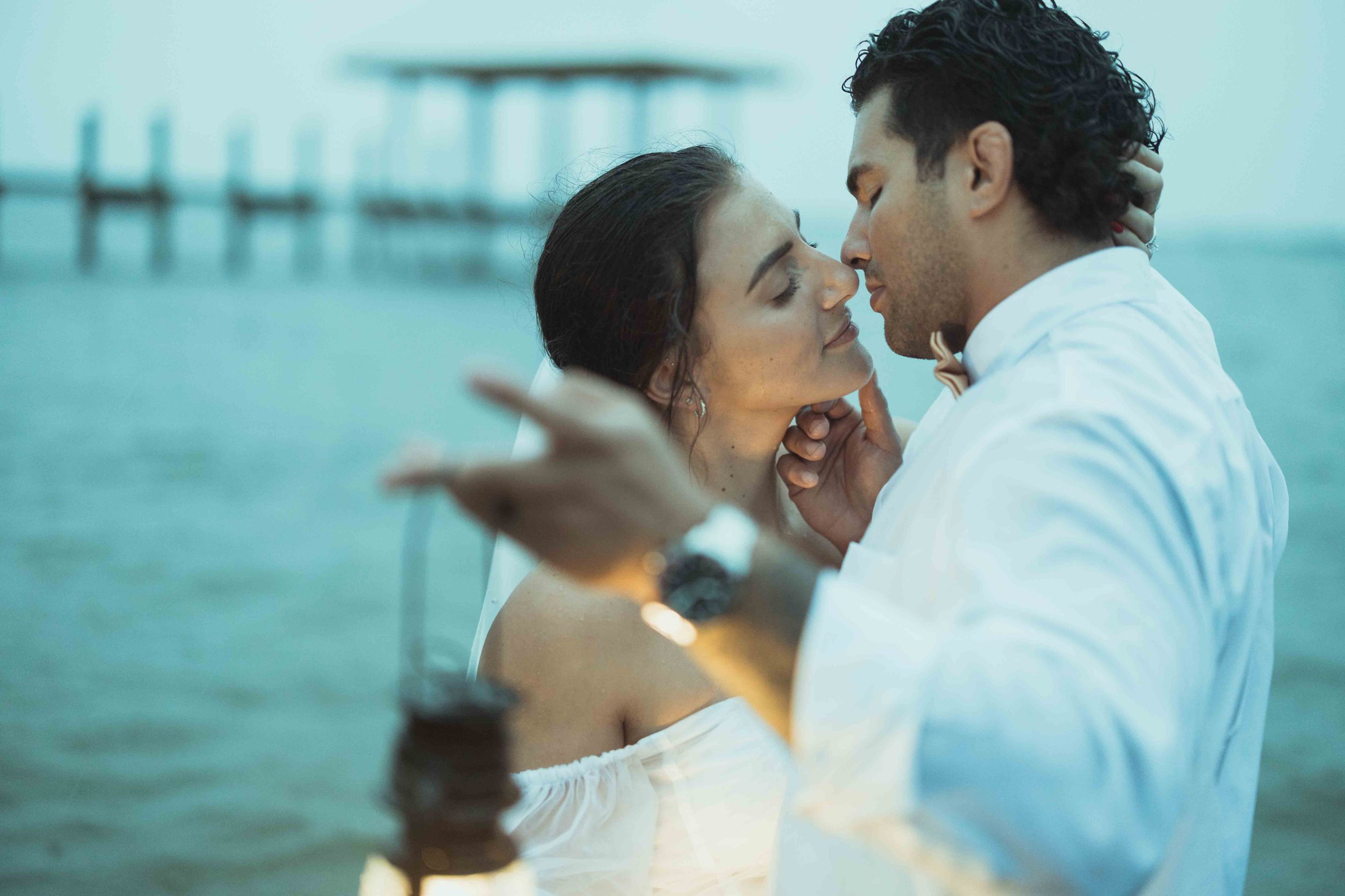 A romantic embrace by the ocean with a pier in the background at dusk.