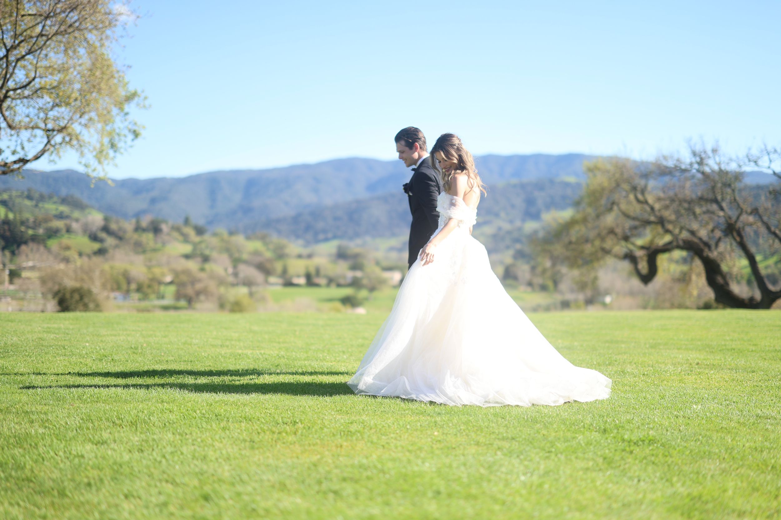 A couple poses on a lush golf course with mountains in background.