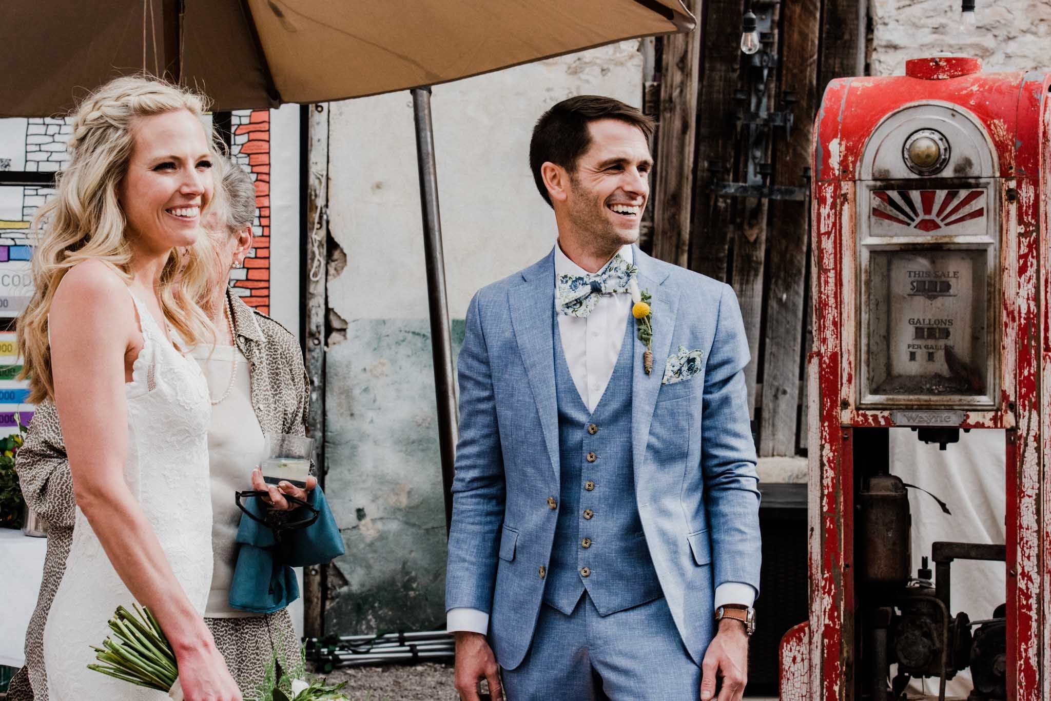 A newlywed couple poses near a vintage red fire alarm in an urban setting.