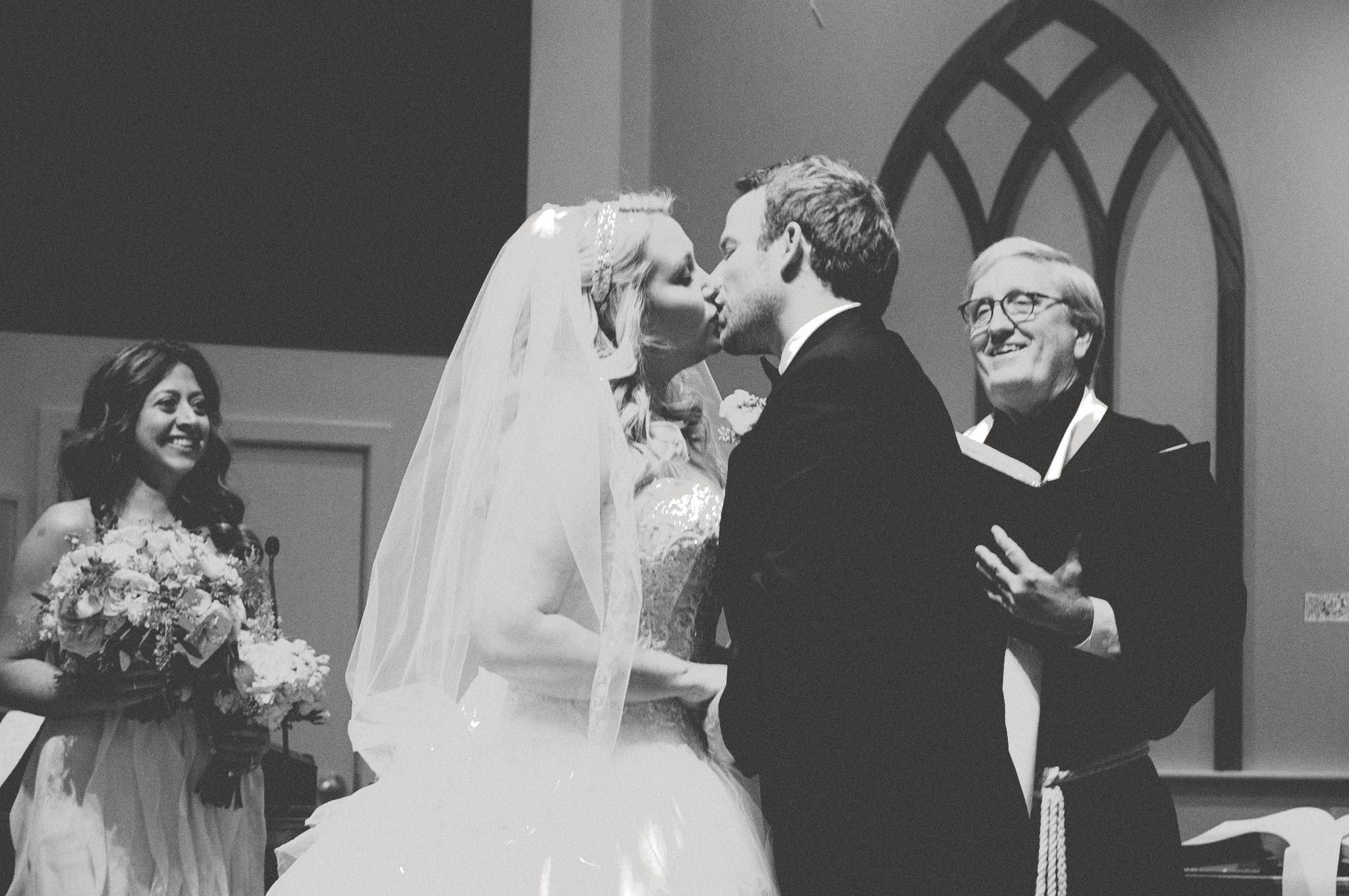 A black and white wedding ceremony photograph captures an intimate moment at the altar.