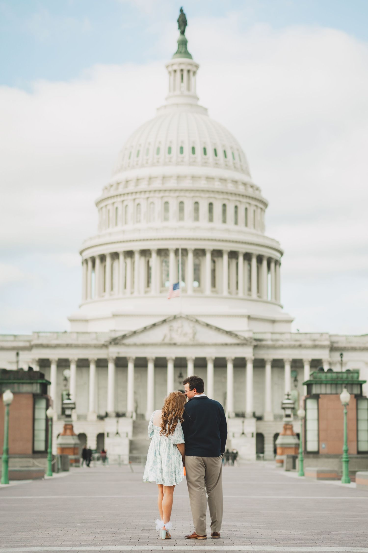A couple walks together on the plaza in front of the United States Capitol Building in Washington DC on a cloudy day.