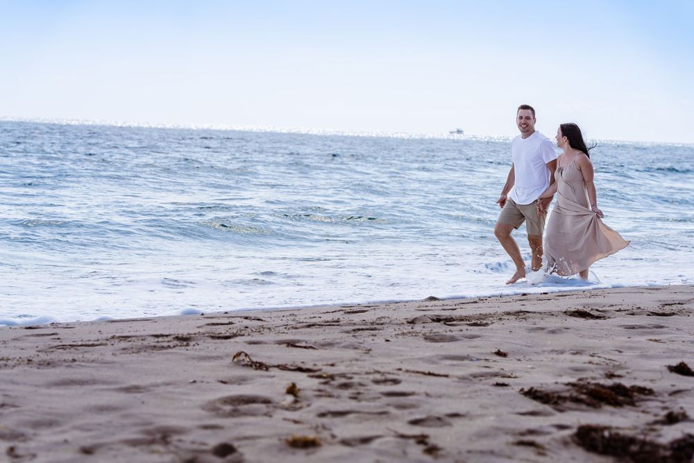 Romantic couple walking along beach shoreline at sunset in casual attire.