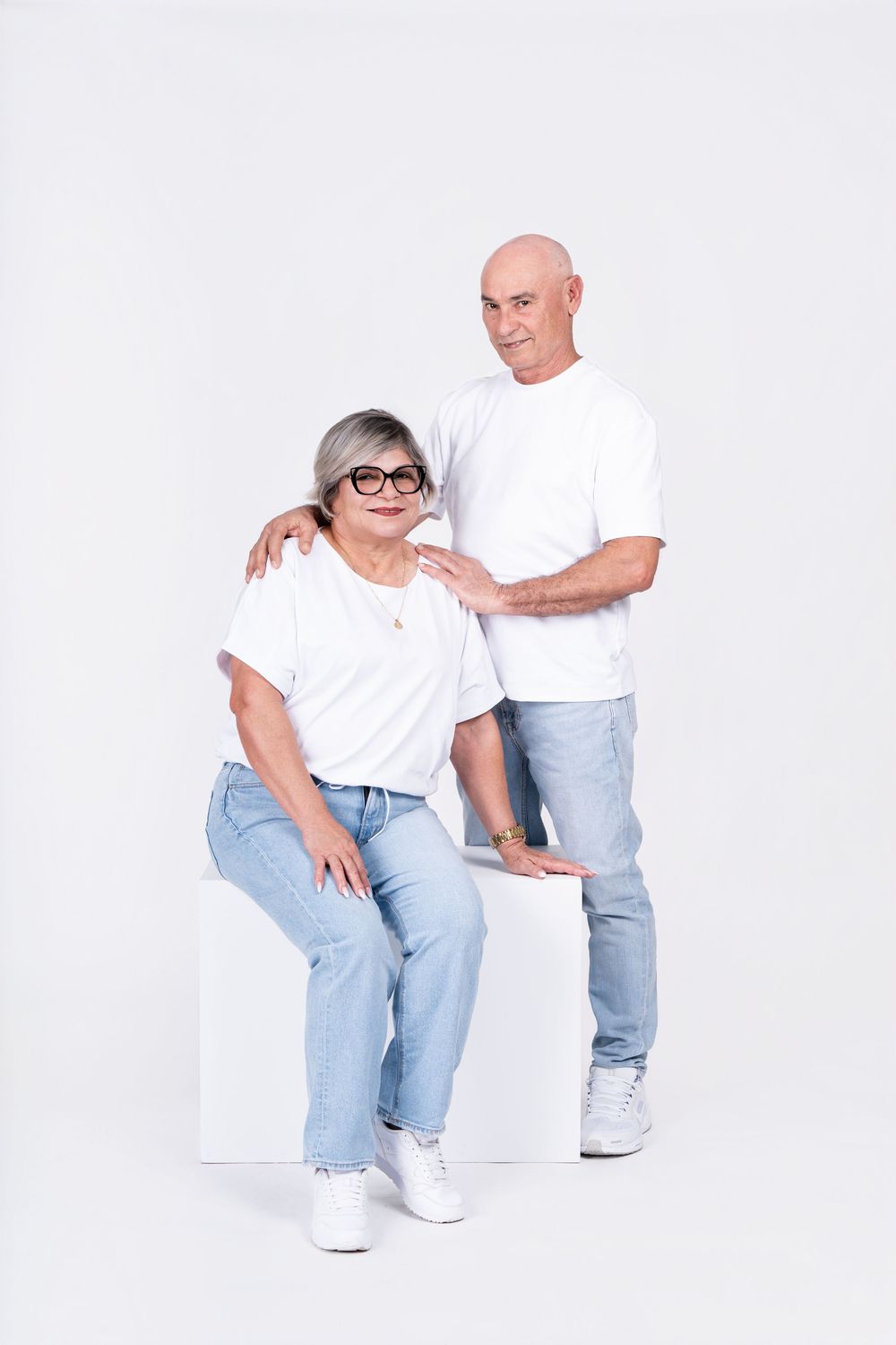 Casual portrait of a senior couple in matching white t-shirts and jeans against white background.